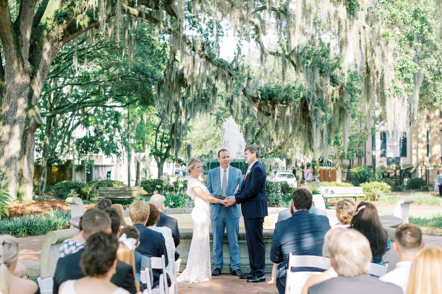 An outdoor wedding ceremony takes place under Spanish moss-draped oak trees in a downtown savannah square during their elopement.