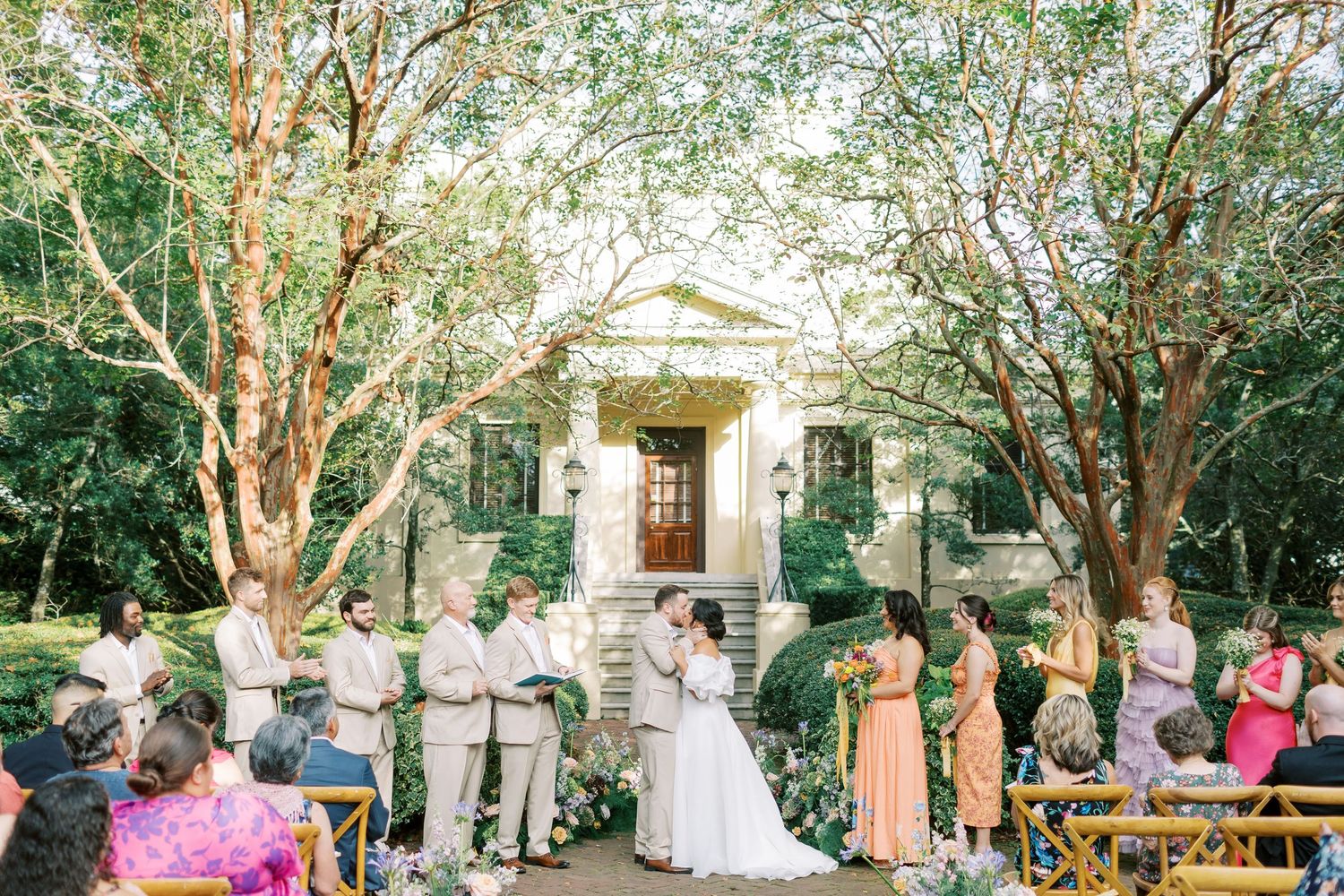Outdoor wedding ceremony in front of historic building framed by beautiful trees.