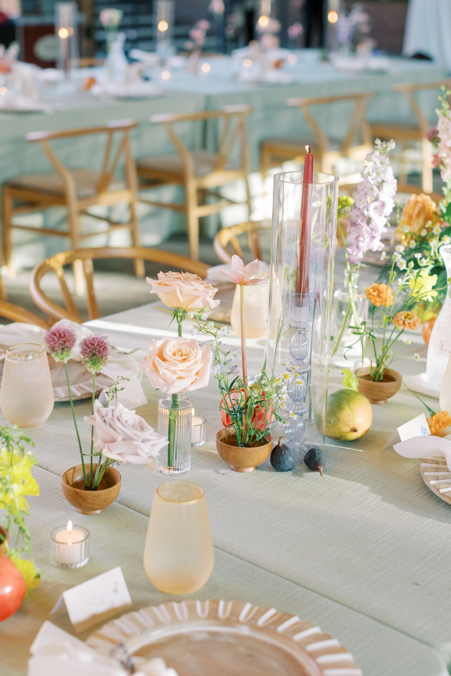 A dreamy tablescape with potted flowers, tall candles, and geometric vases on a sage green tablecloth.