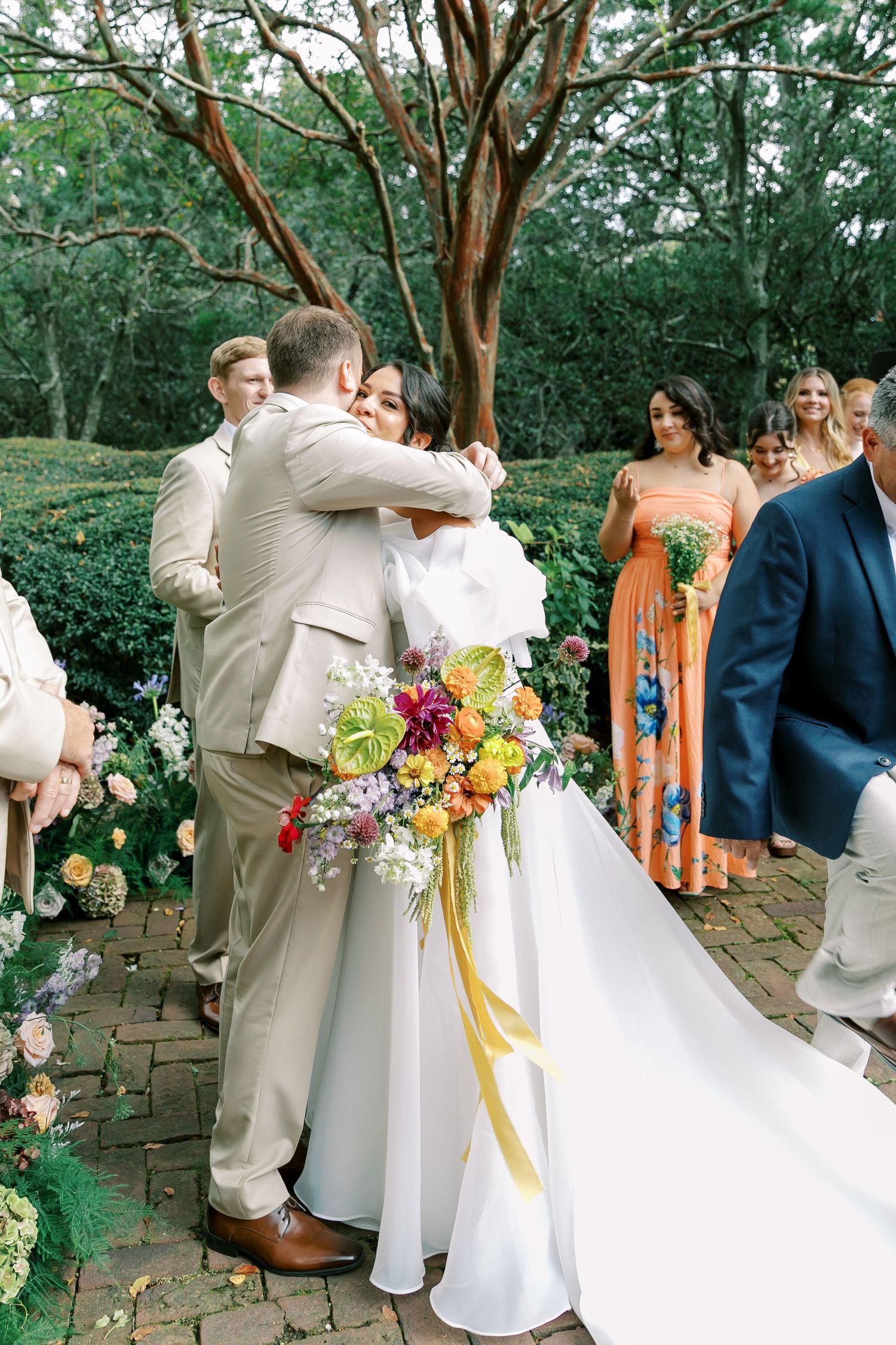 Wedding celebration with bridal party in colorful dresses on brick garden pathway.