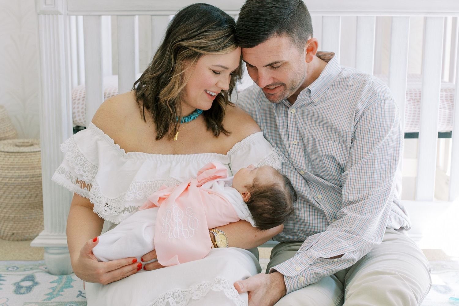 Parents lovingly gaze at their newborn baby while sitting together in a nursery with white decor.