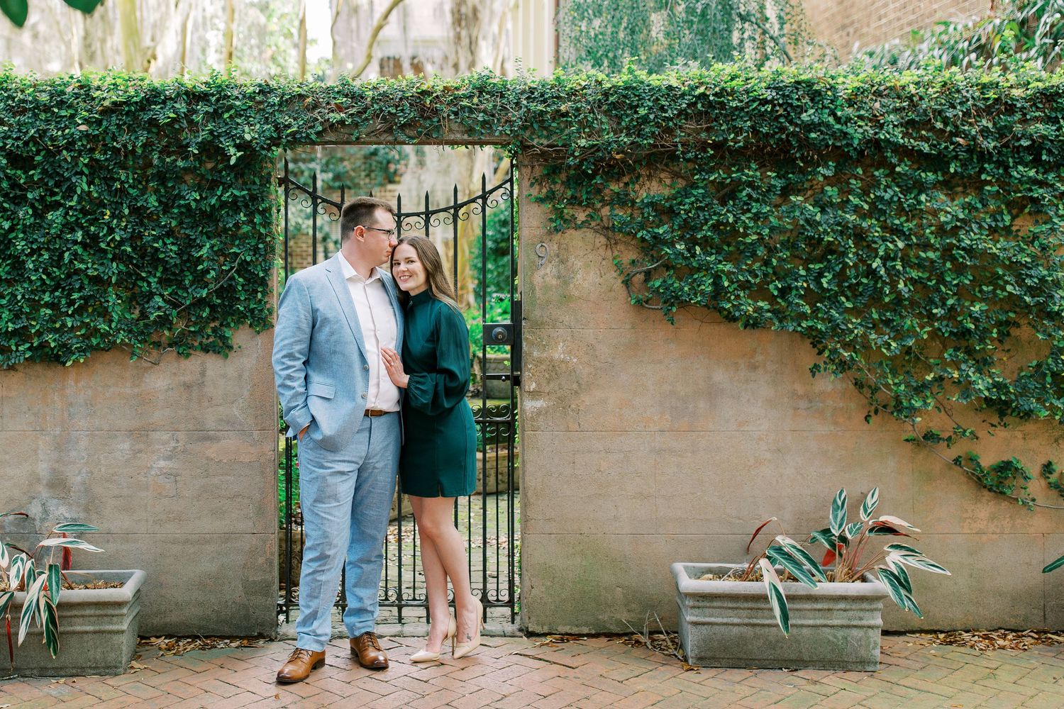 A couple poses by an ivy-covered wall and garden gate in a romantic courtyard setting.
