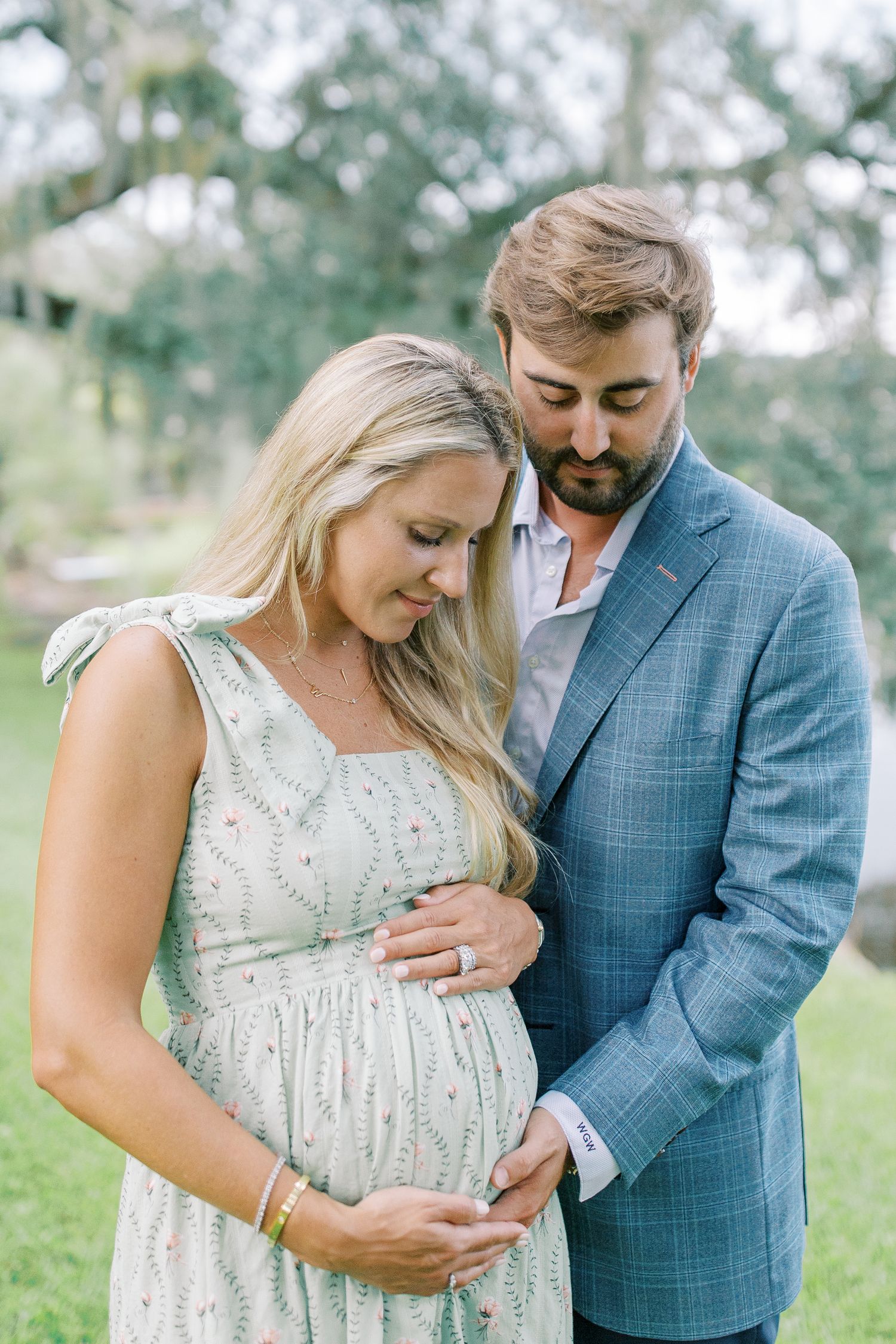 A couple shares an intimate moment while cradling a baby bump under Spanish moss-draped trees.