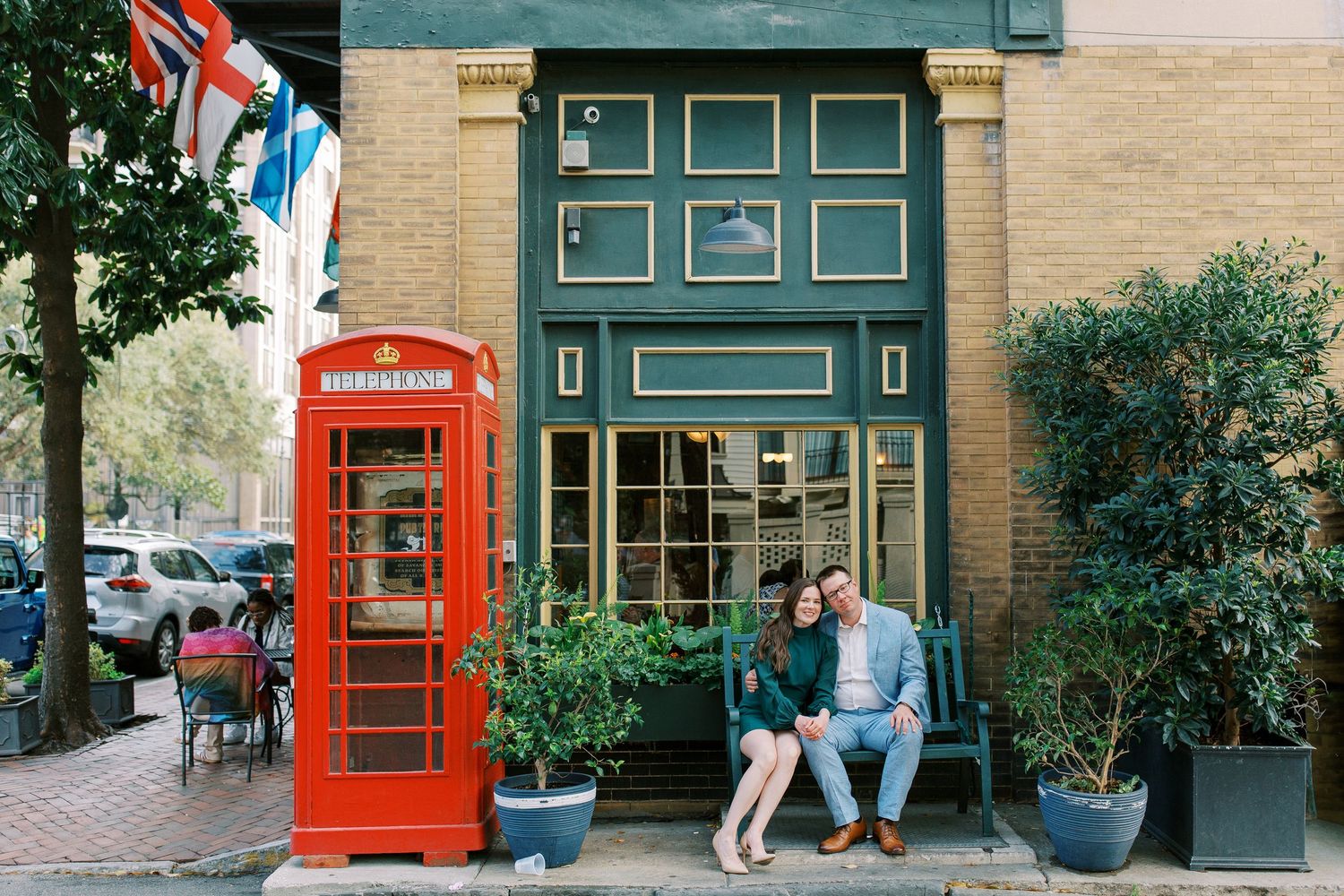 A couple sits near a classic red British phone booth outside a charming storefront.