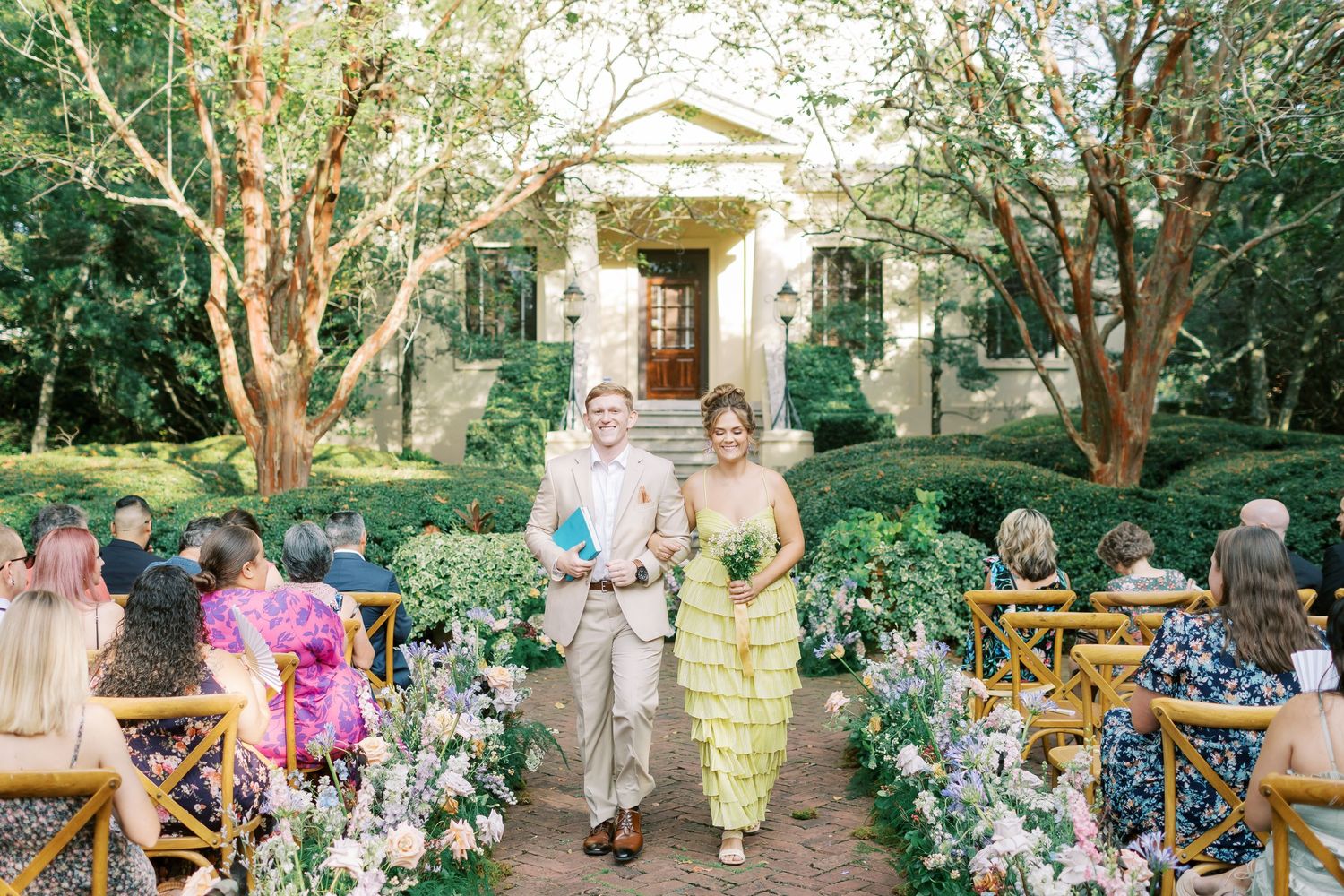 Wedding guests gather on a garden path for group photos during an outdoor celebration.