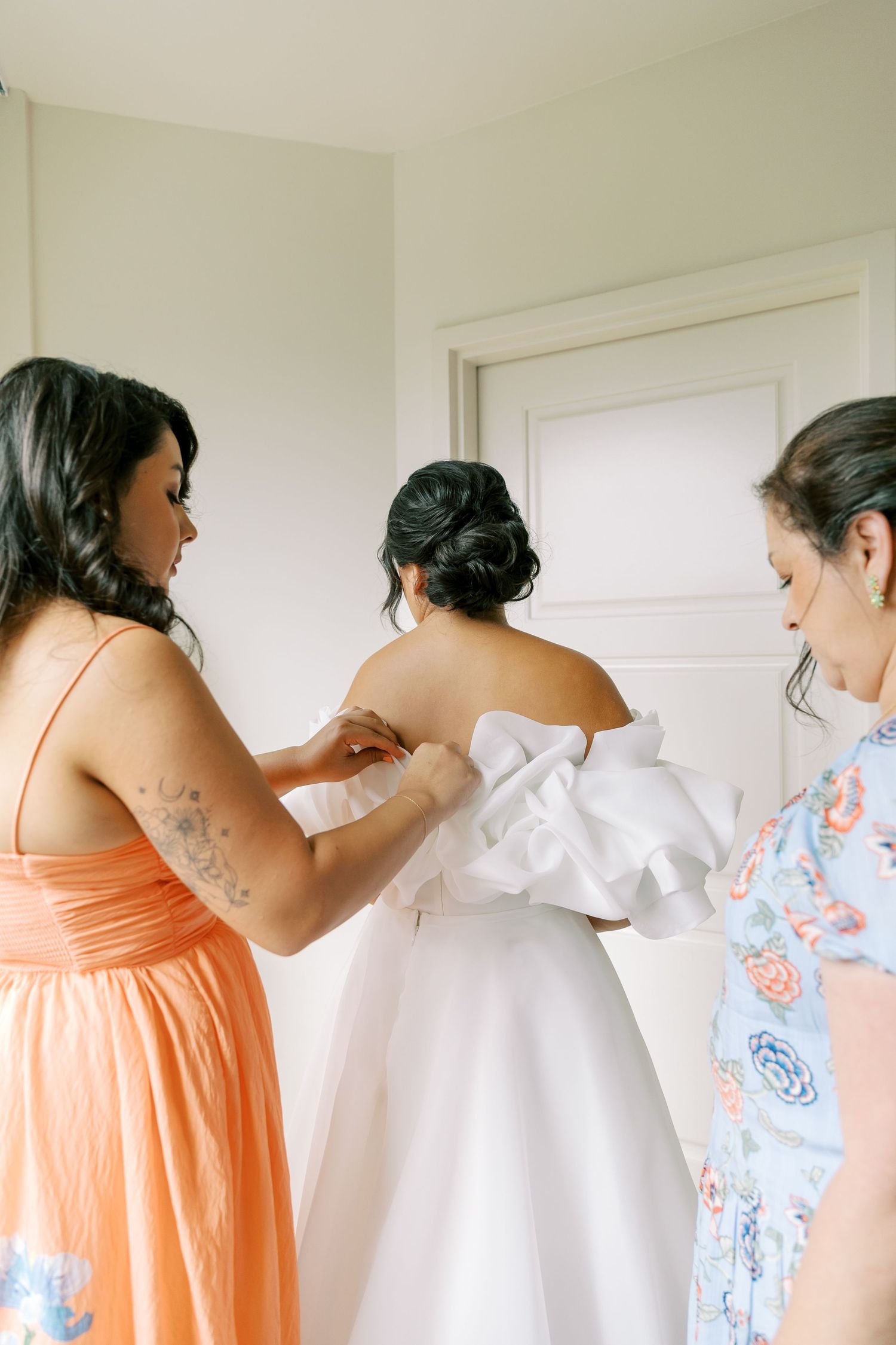 Bridesmaids in peach and floral dresses help adjust a wedding gown during pre-ceremony preparations.