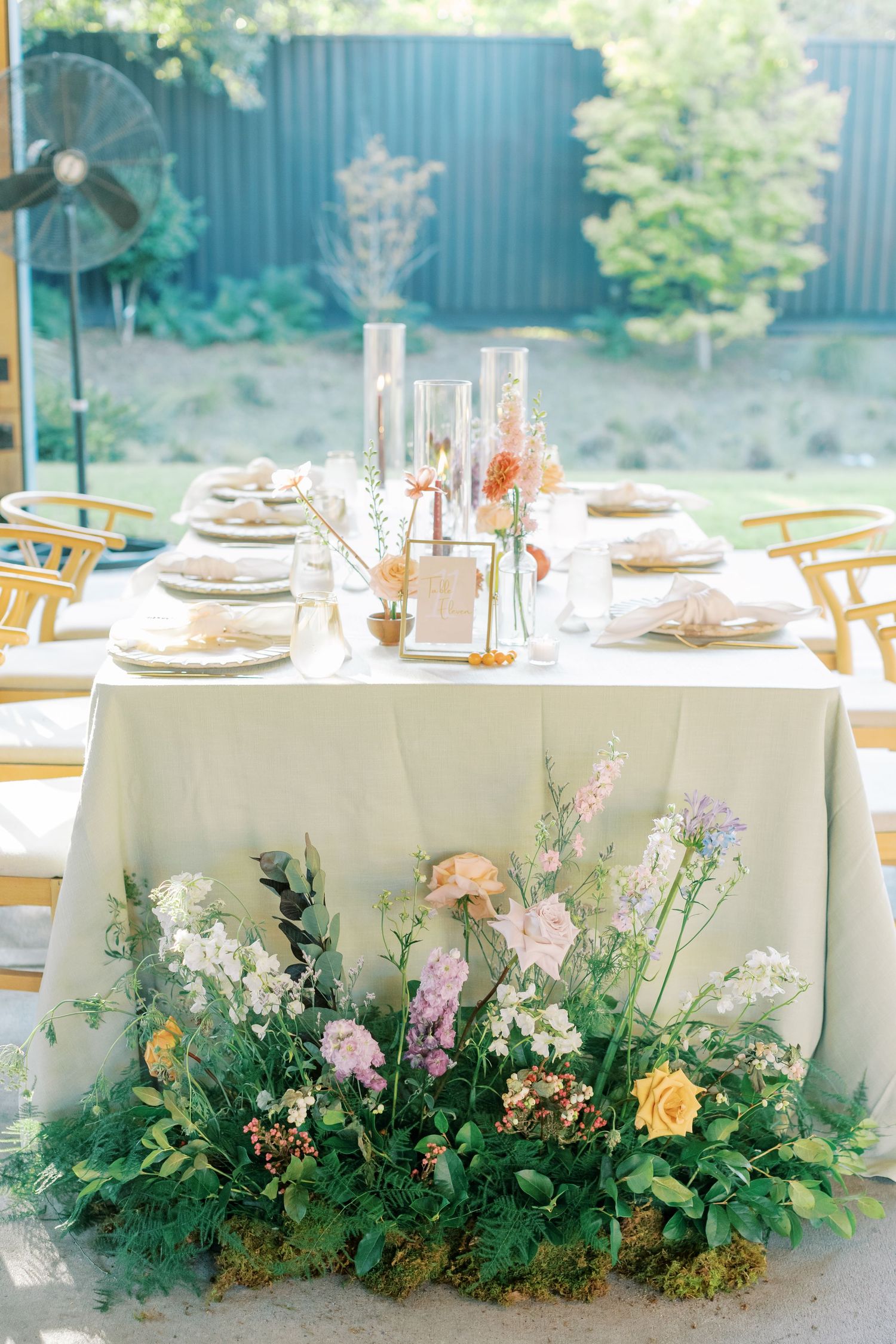 Long reception tables with lush greenery and floral arrangements running along white tablecloths.