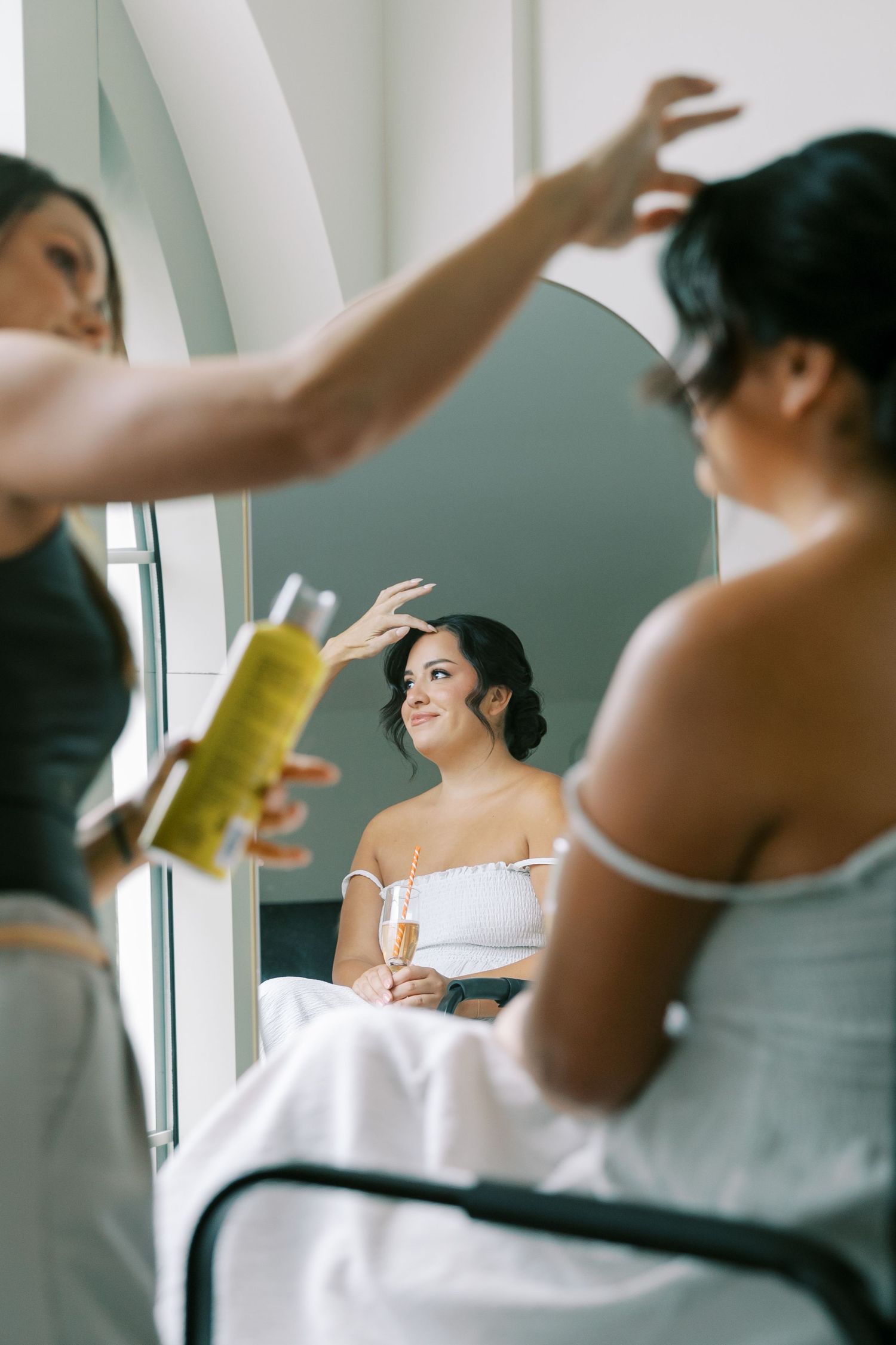 Wedding preparation scene shows people getting ready in a bright room as hairspray is being applied.