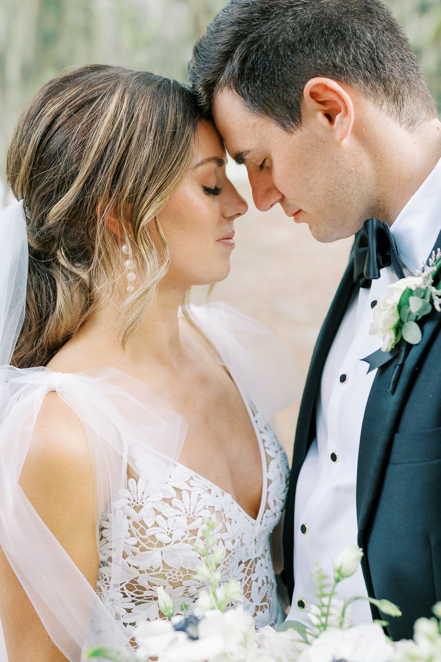 A romantic wedding photo showing a tender moment between newlyweds in formal attire with soft lighting and floral details.