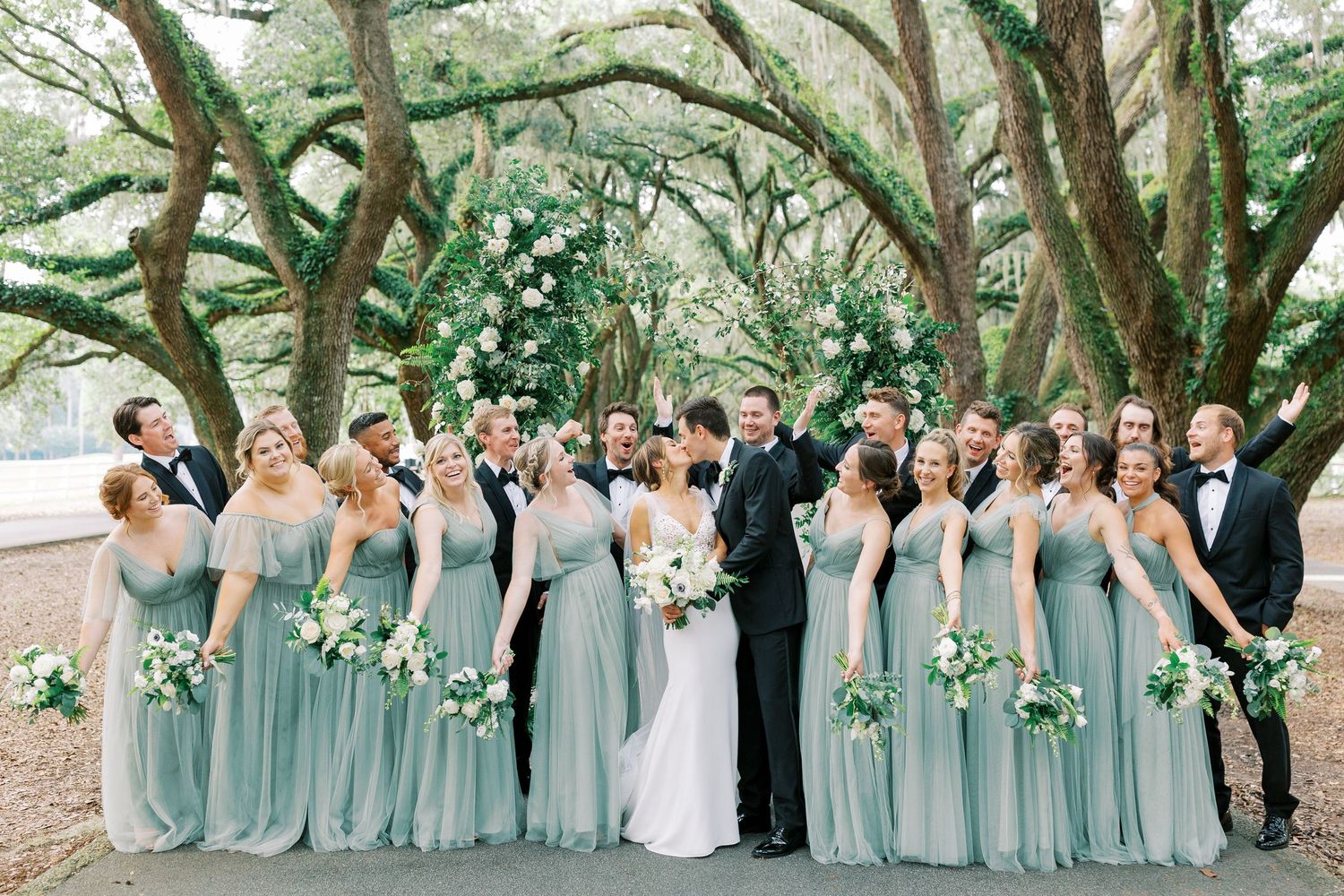 Wedding party wearing seafoam green dresses posed under mossy oak trees at an outdoor venue.