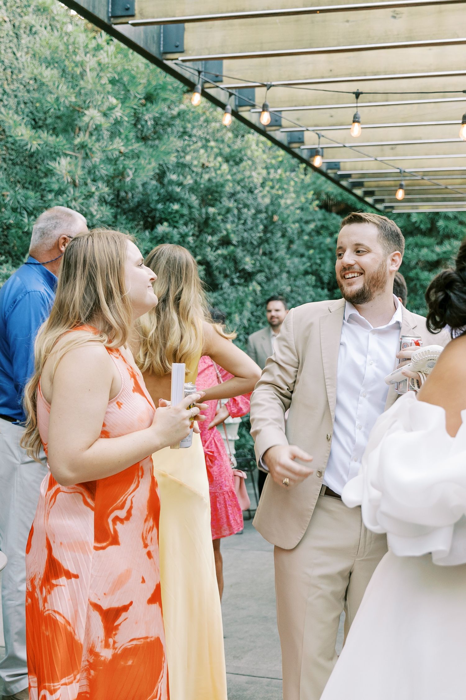 A festive outdoor wedding reception with string lights and guests in colorful attire.