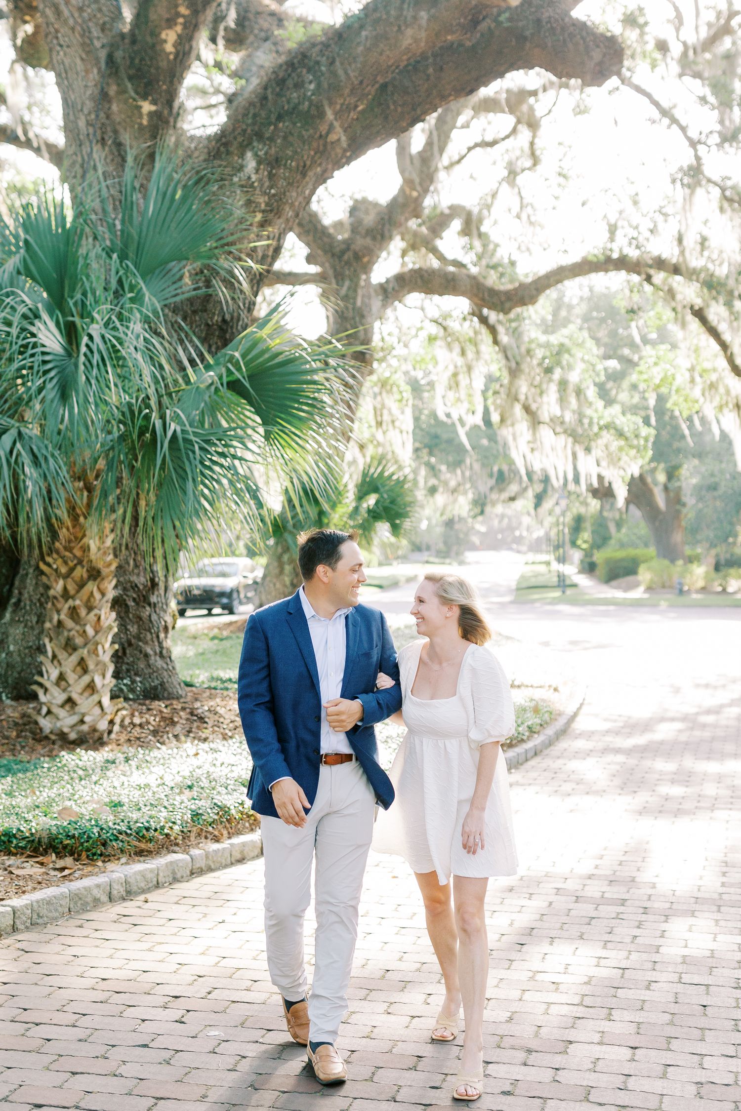 Couple walking on a brick lined road with palm trees and spanish moss hanging in palmetto bluff.