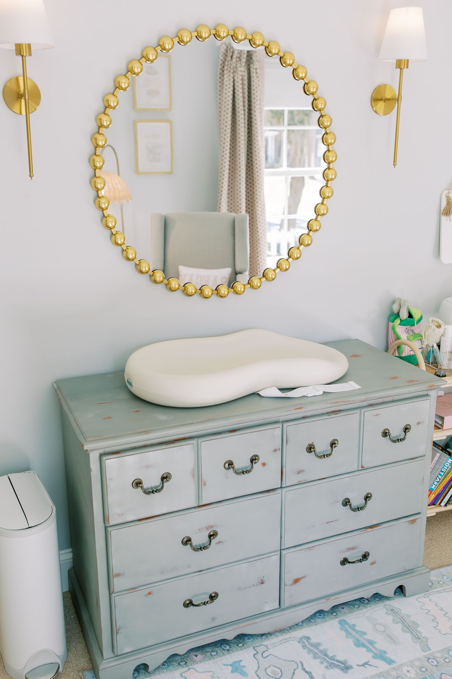 Vintage-style nursery dresser with gold beaded mirror and white changing pad in a soft blue and white color scheme.