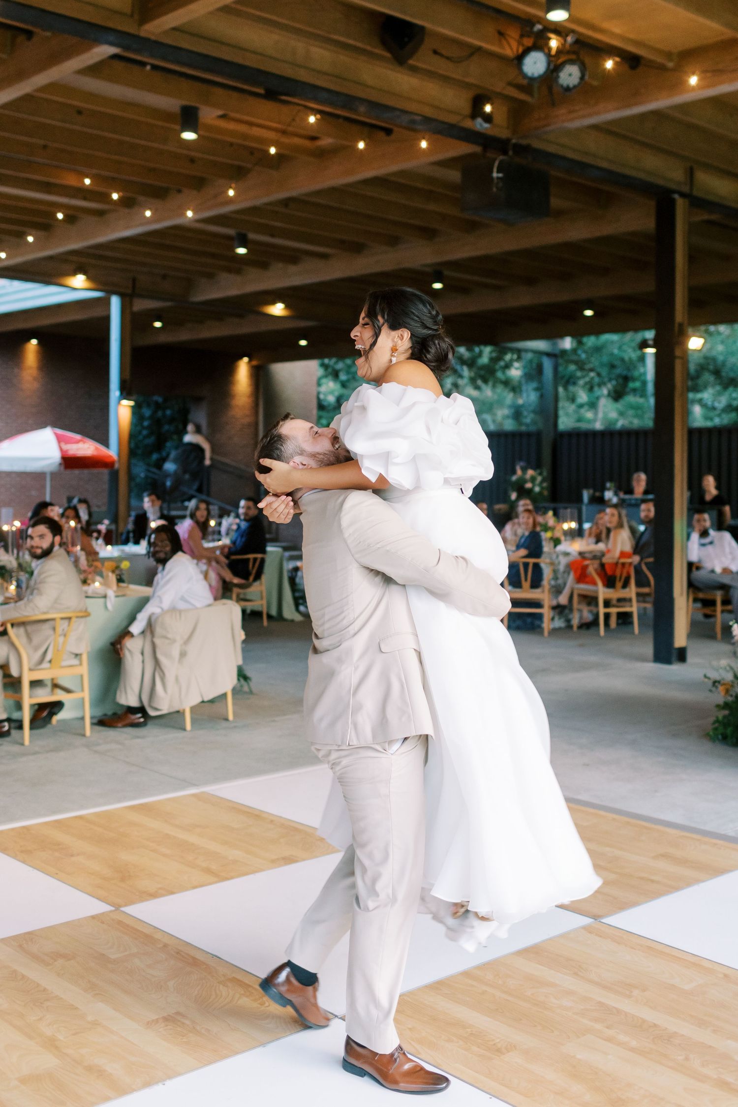 Wedding guests dancing and celebrating on a wooden dance floor under a covered outdoor venue.