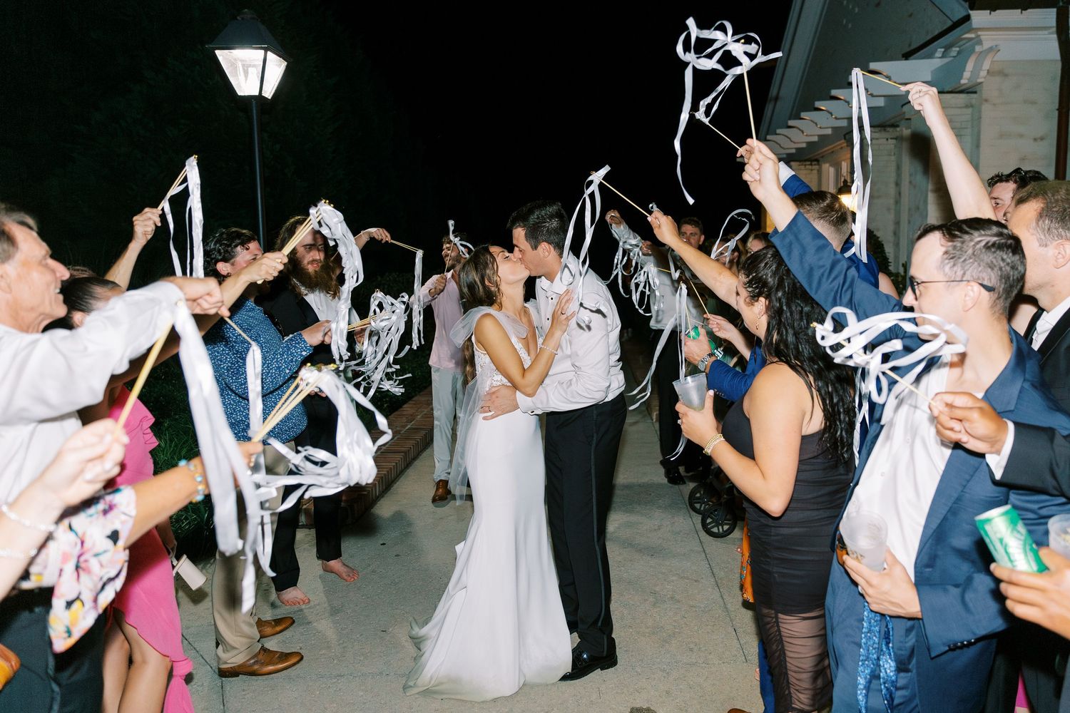 Wedding exit celebration with guests waving white ribbons at night.