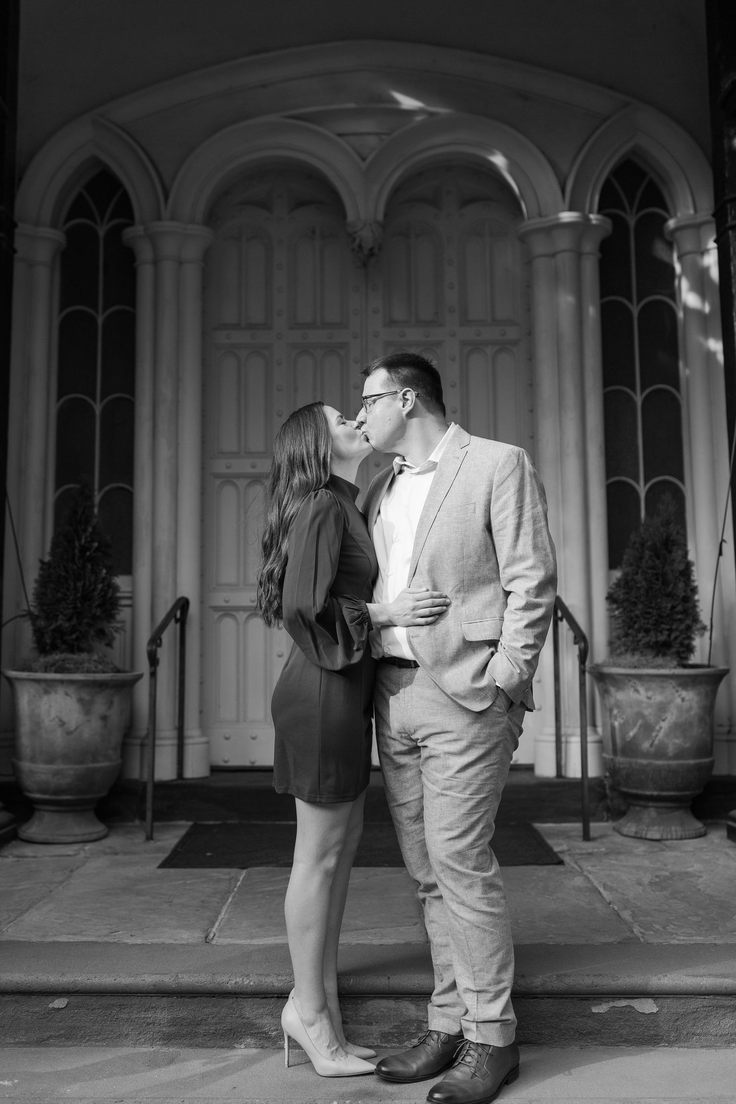 A black and white portrait of a couple in an intimate moment by an ornate doorway.