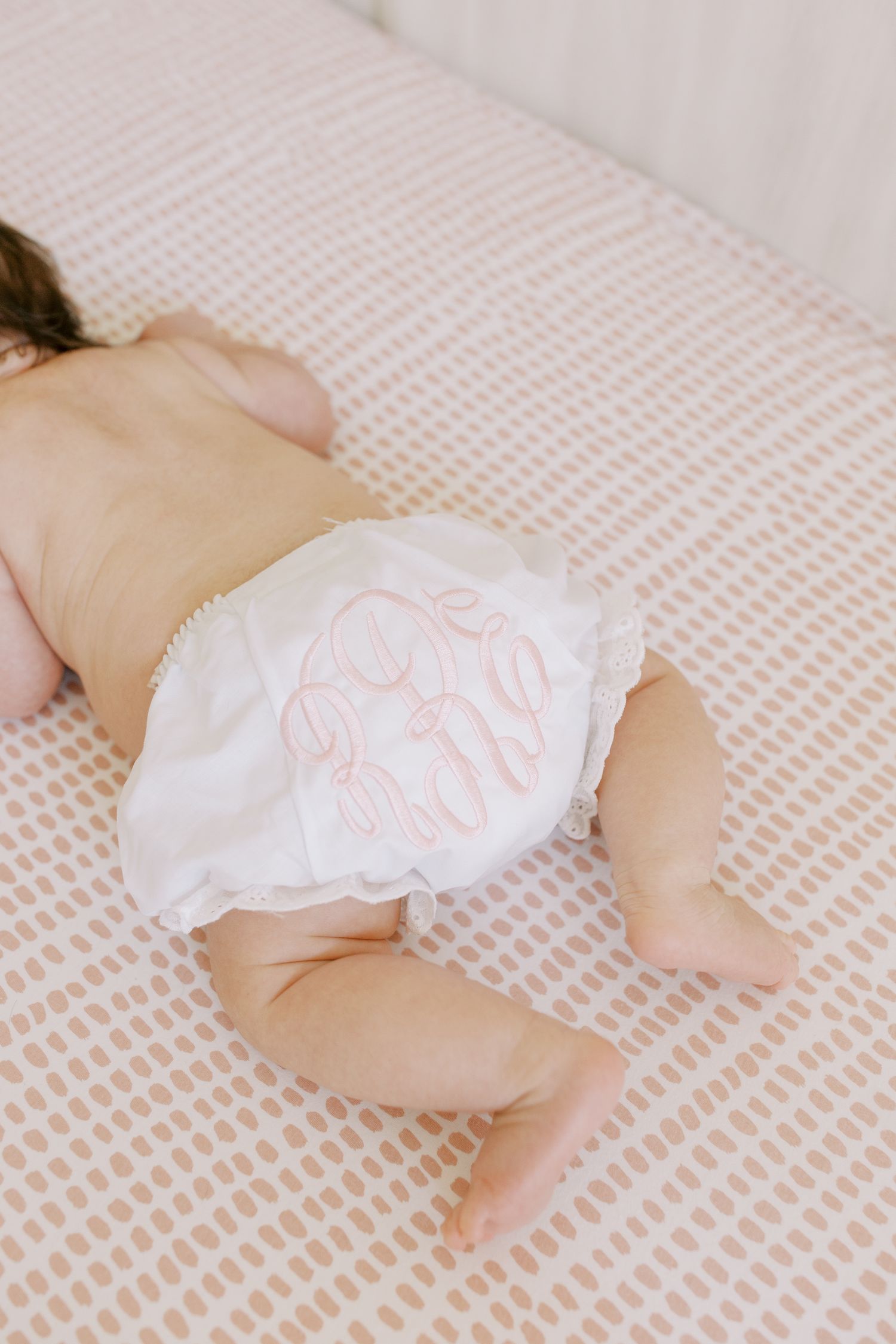 Baby wearing monogrammed white diaper lying on textured pink bedding.