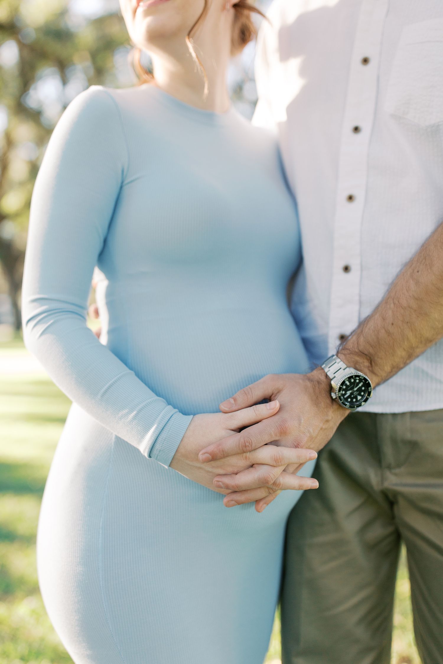 Close-up of couple holding hands outdoors with person wearing light blue fitted dress and partner in white button-down shirt.