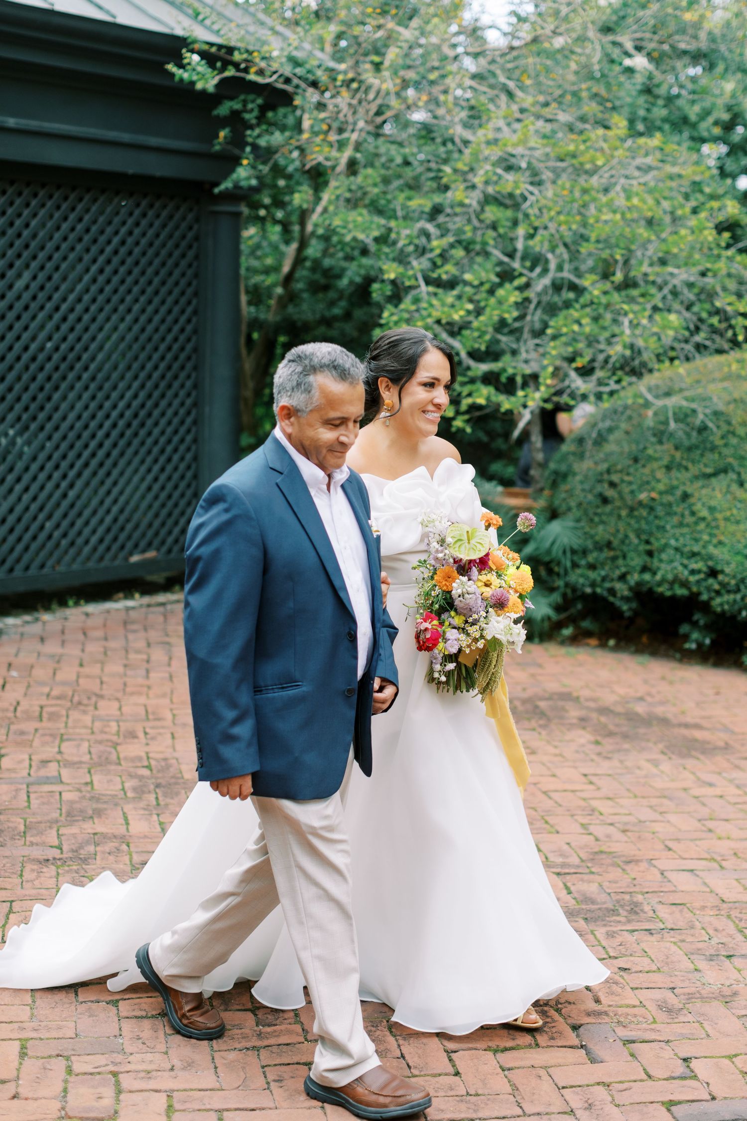 A white wedding dress and colorful floral bouquet on display in a garden setting with brick pathways.