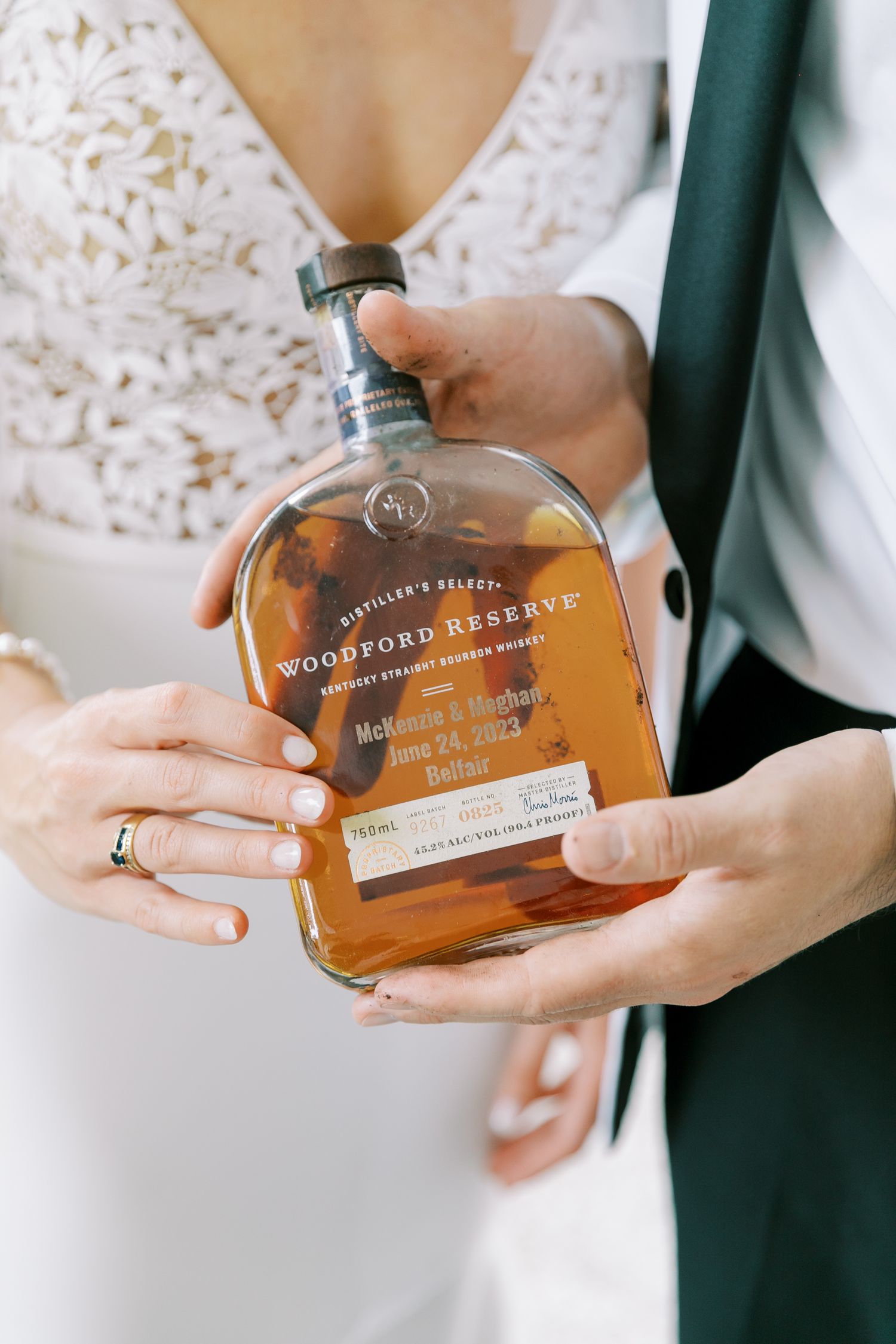 Someone in a white lace dress and green jacket holds a bottle of Woodford Reserve bourbon whiskey.