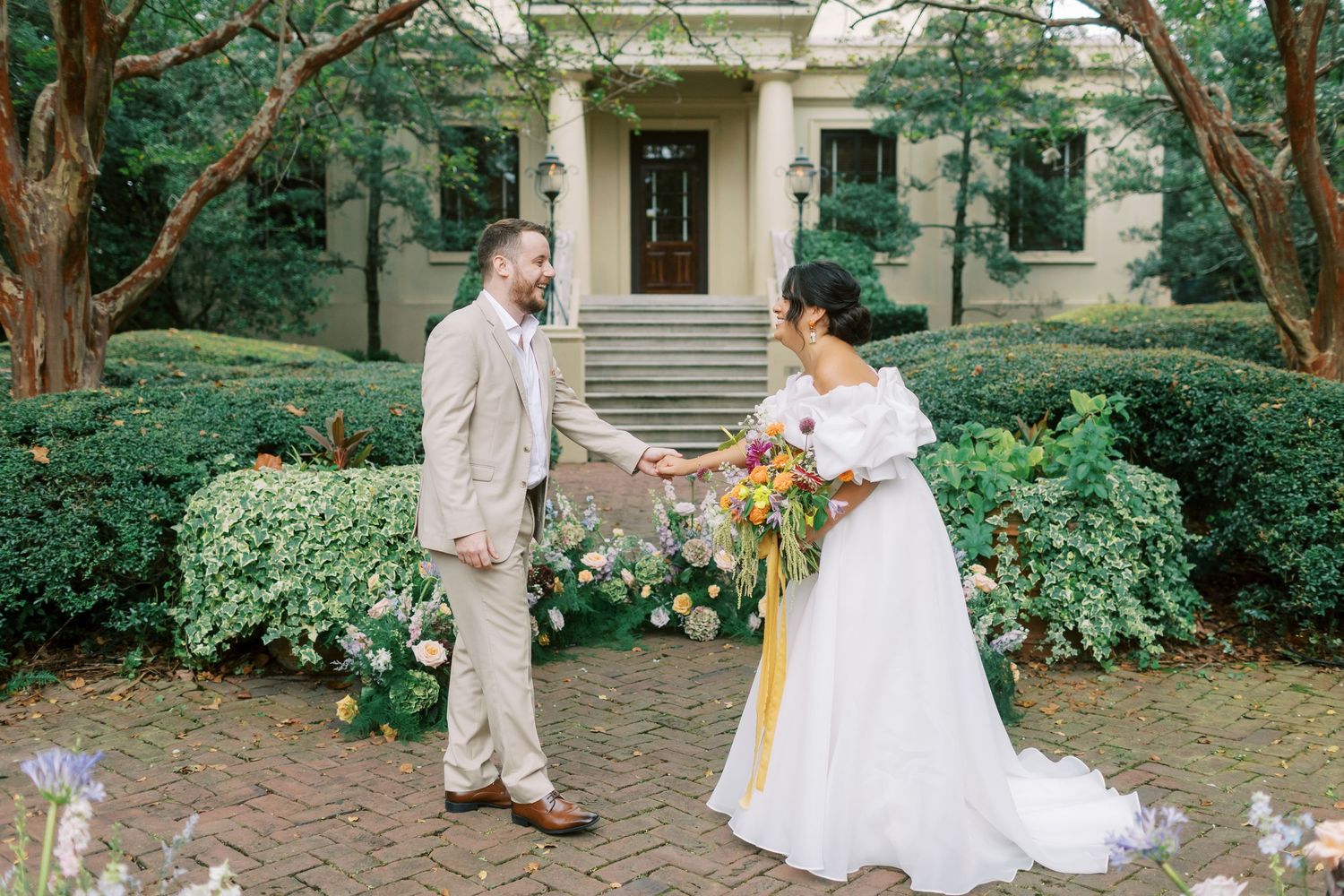 A couple shares a laugh during their outdoor wedding ceremony in front of a historic building.