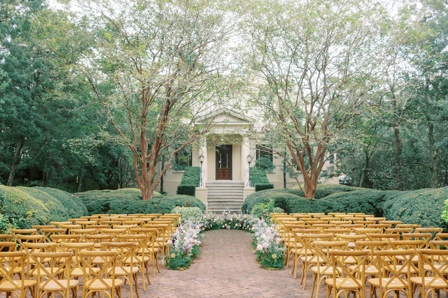 Outdoor wedding venue with rows of golden chairs leading to a classic white building entrance.