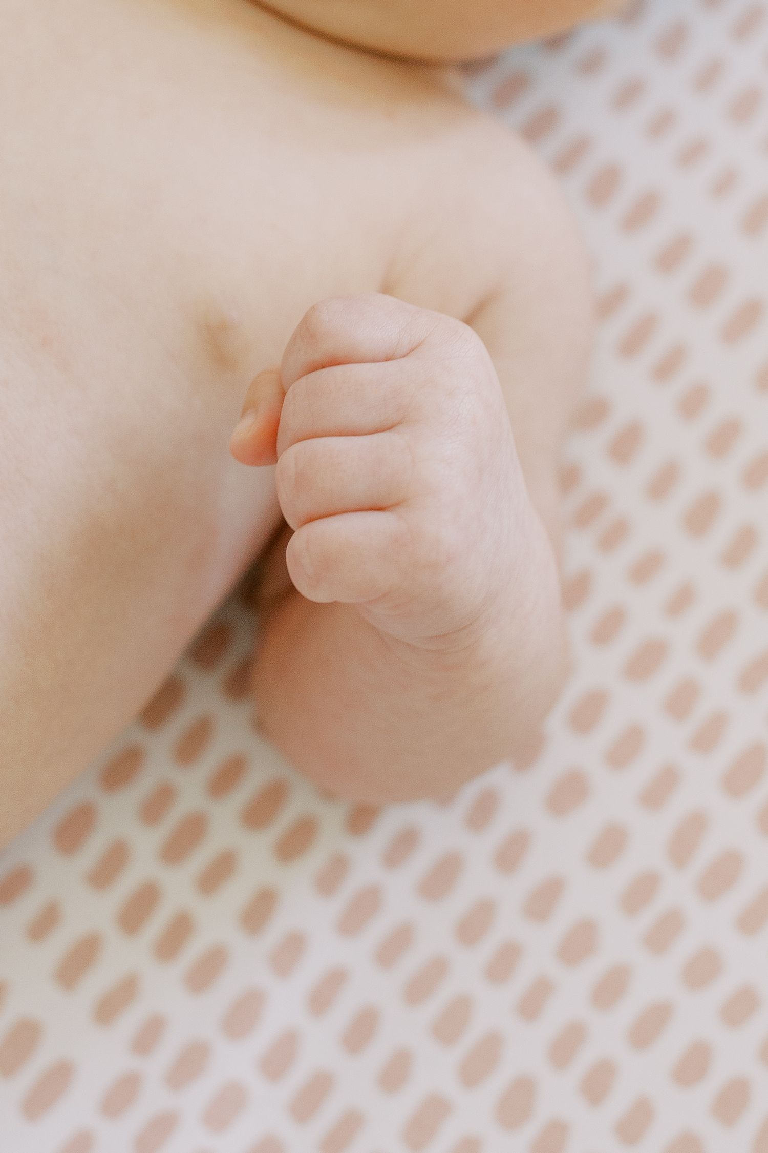 Close-up of tiny baby hand against textured pink background.