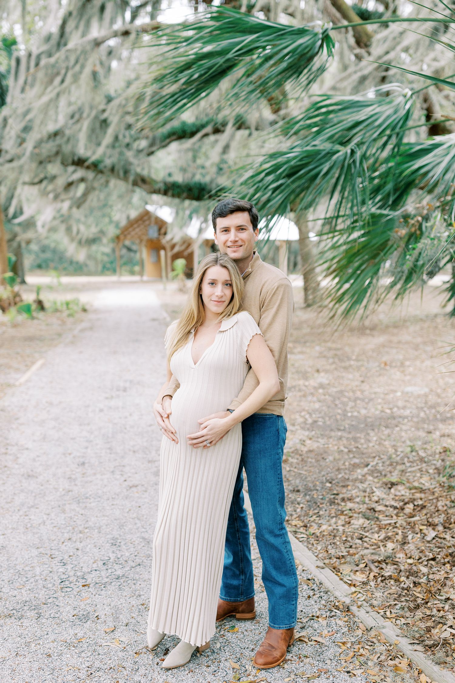 Couple standing on a gravel path under palm trees at a romantic outdoor location on a sunny day.