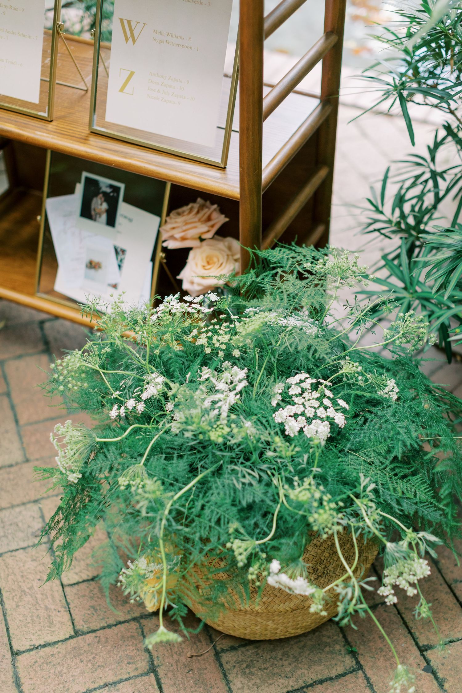 Delicate arrangement of wispy green foliage and white flowers in a woven basket against wood shelving.