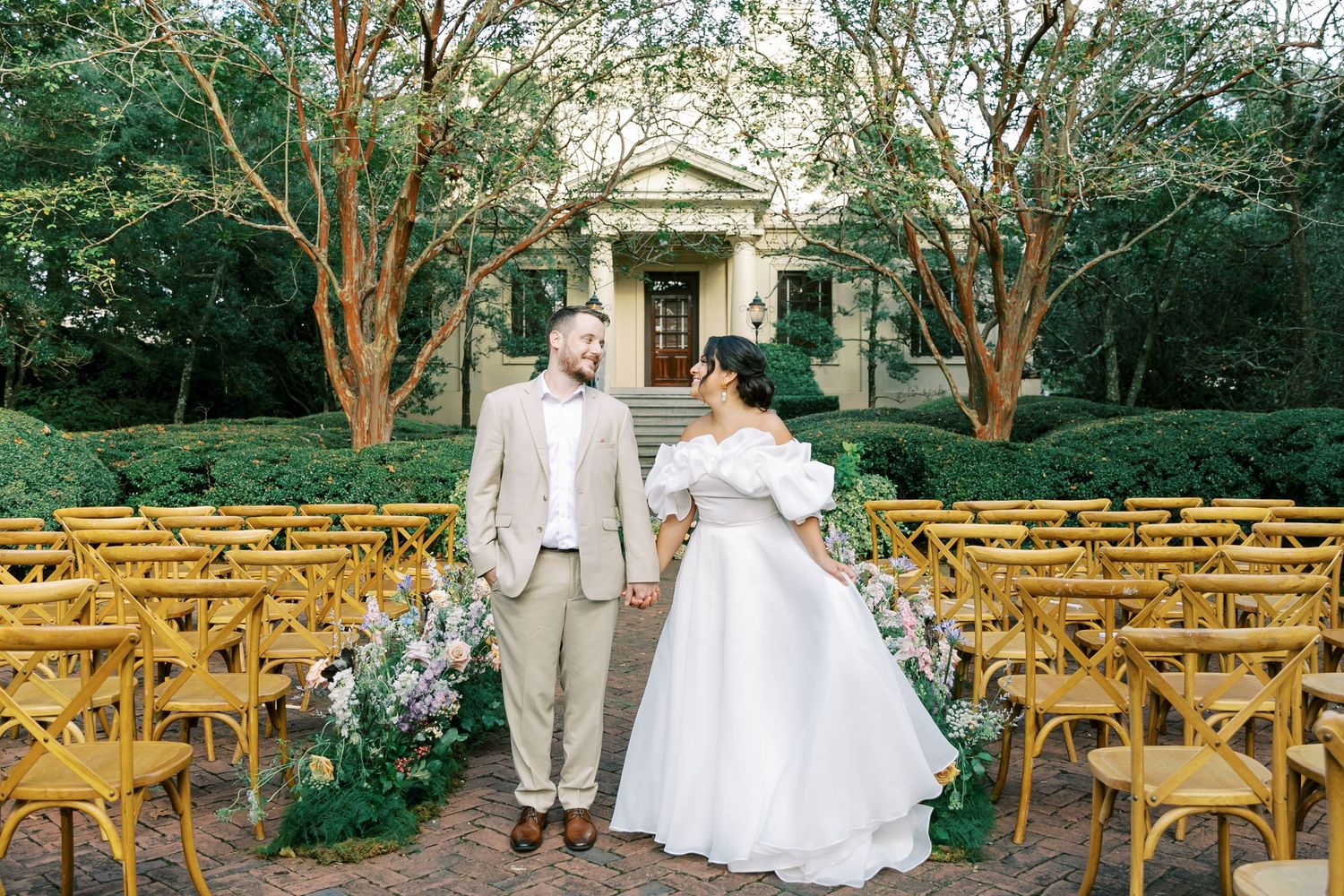 A romantic outdoor wedding scene with wooden chairs and floral arrangements in front of a classic stone building.