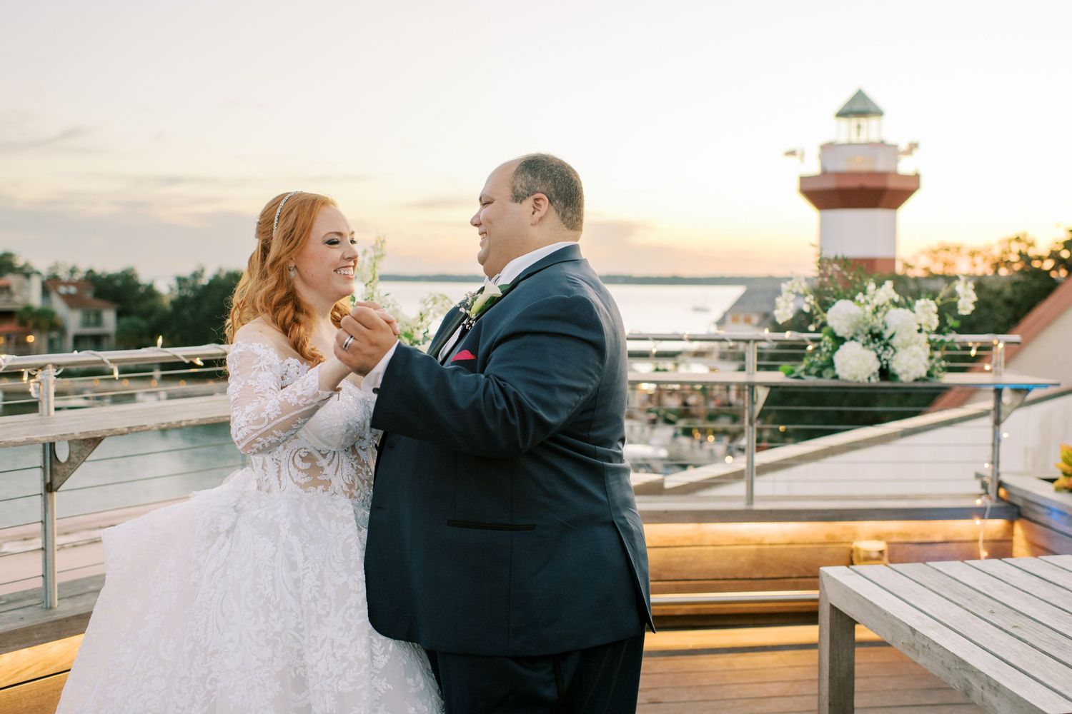 A couple shares an intimate moment on outdoor deck at Harbor Town Lighthouse during sunset wedding celebration.