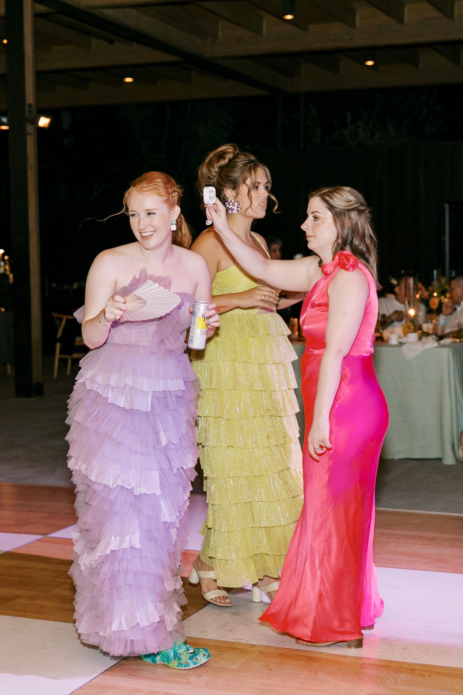 Three women in colorful formal dresses dancing together at a wedding reception.