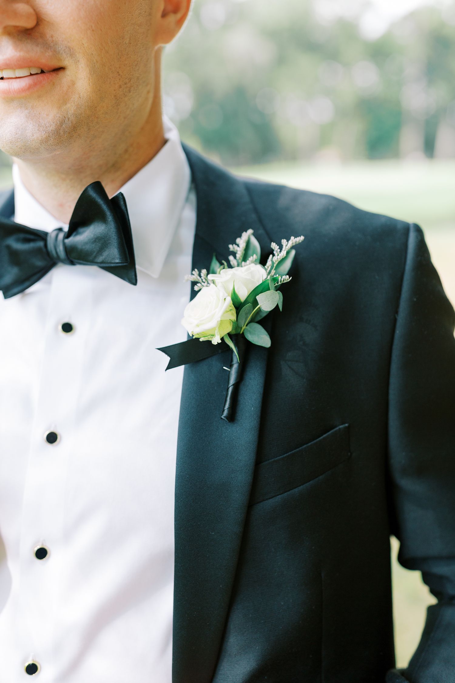 Close up of black tuxedo with white boutonniere and bow tie.