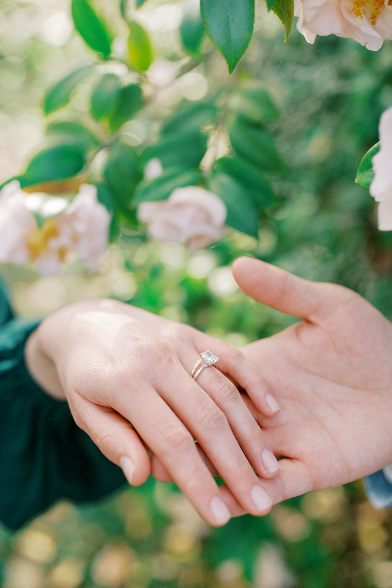 Close up of engagement ring on hand with soft focus flowers in background.