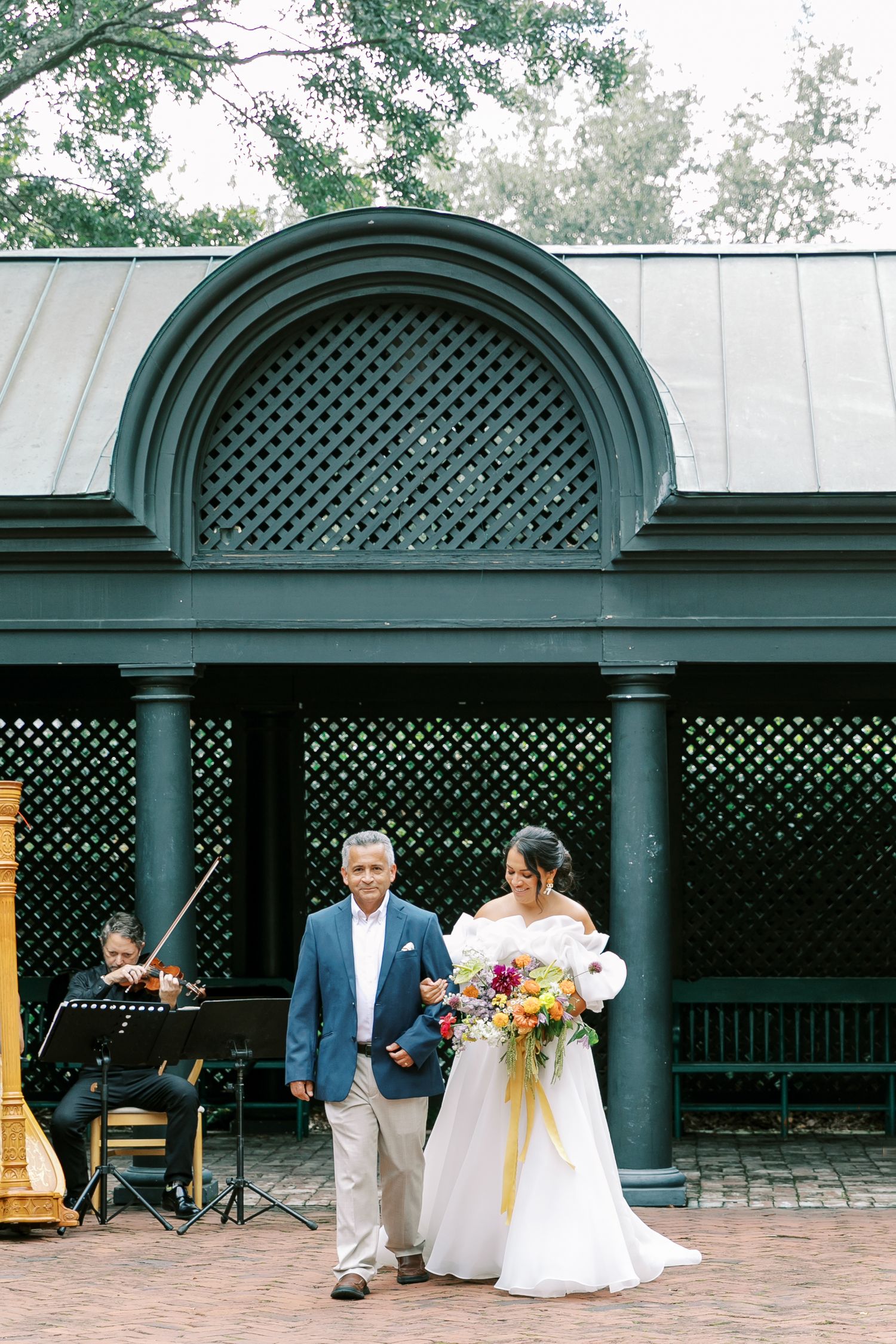 Wedding scene under a latticed gazebo with live musician playing piano in the background.
