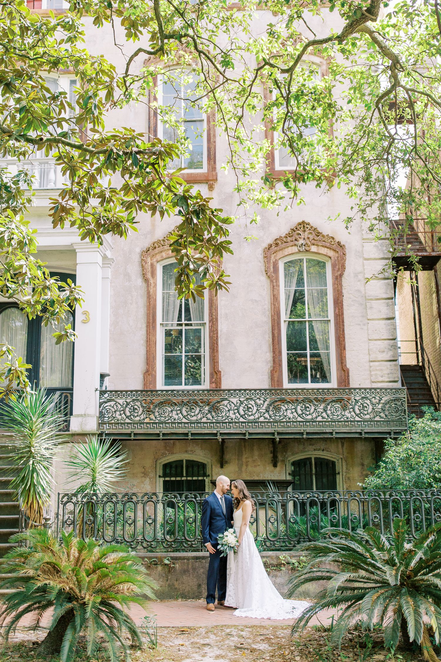 A bride and groom pose in front of a historical building in downtown savannah