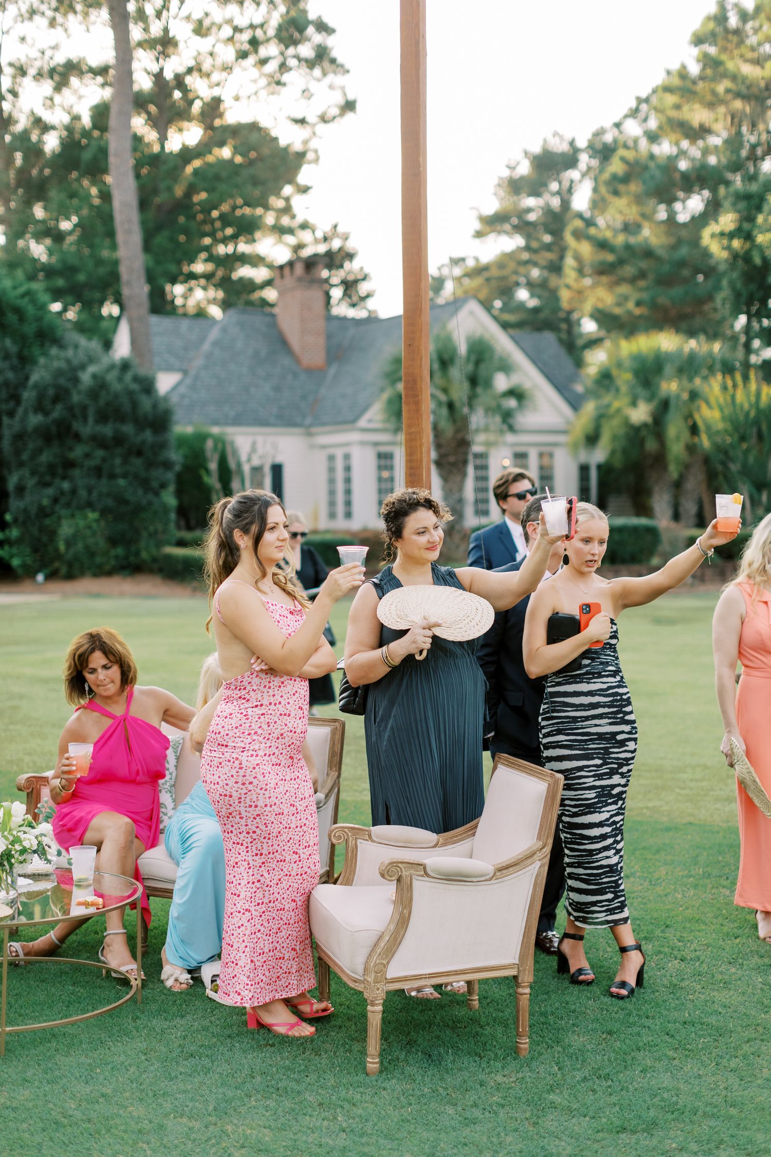 Wedding guests enjoying drinks and taking photos on an elegant lawn during an outdoor reception.