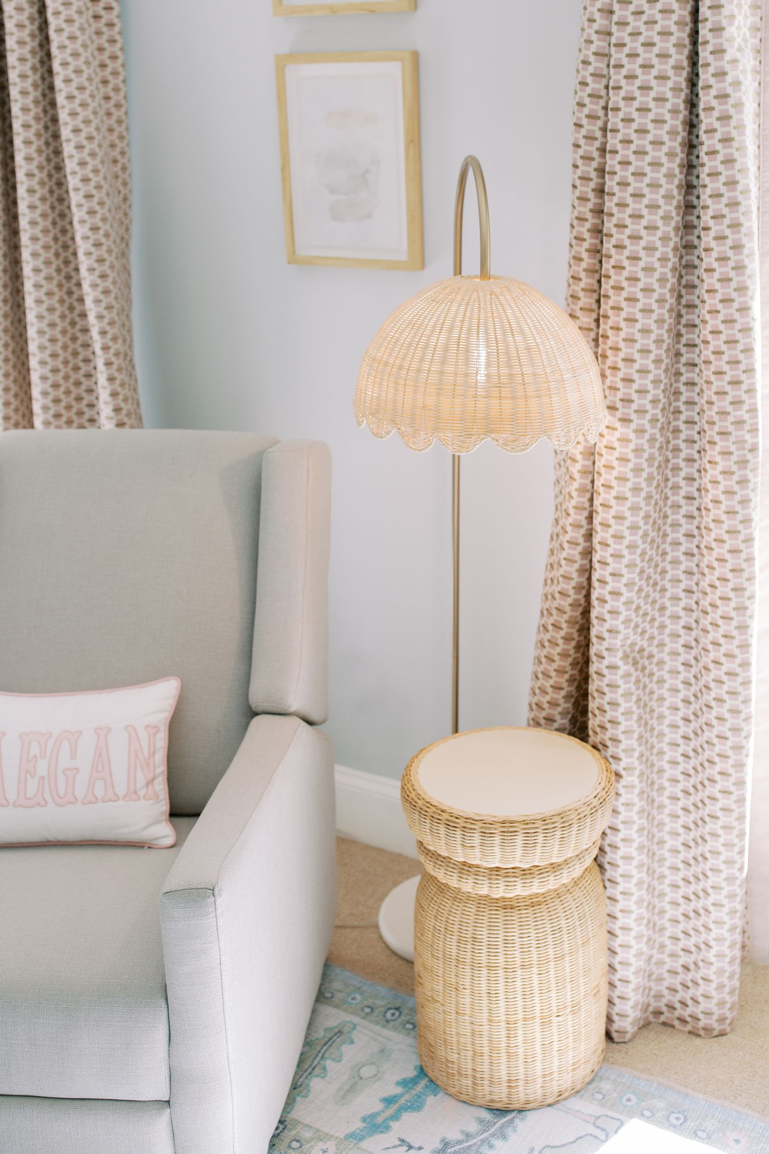Light and airy nursery corner with woven rattan lamp and stool next to a gray armchair and polka dot curtains.