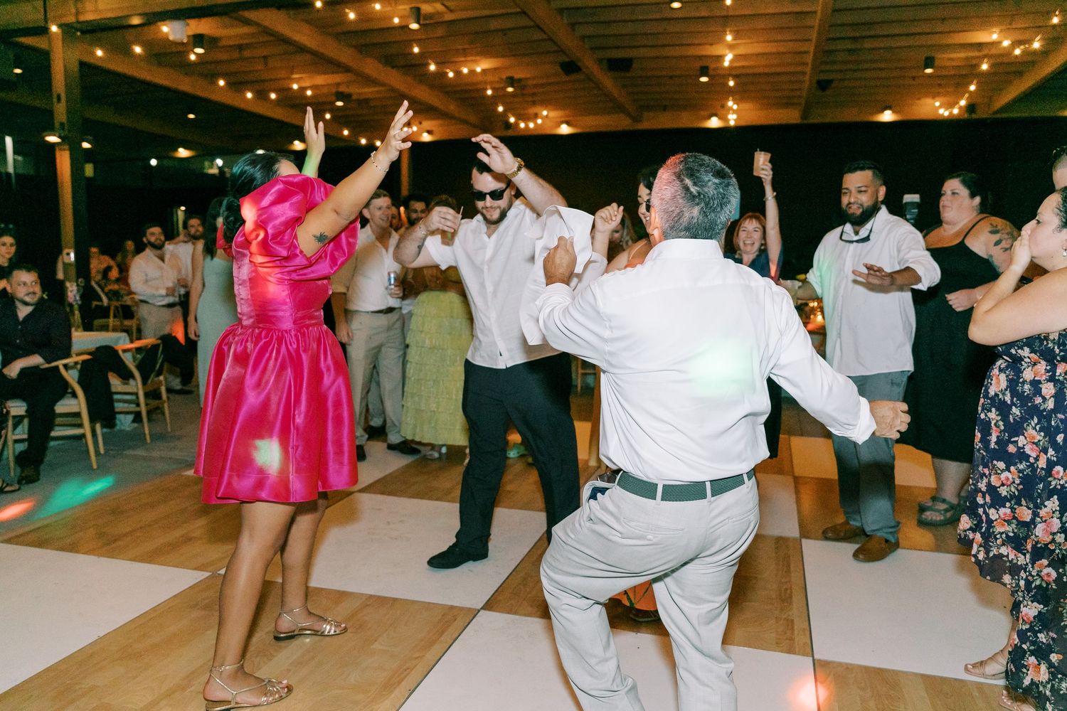 Wedding reception dance party with guests celebrating under string lights.