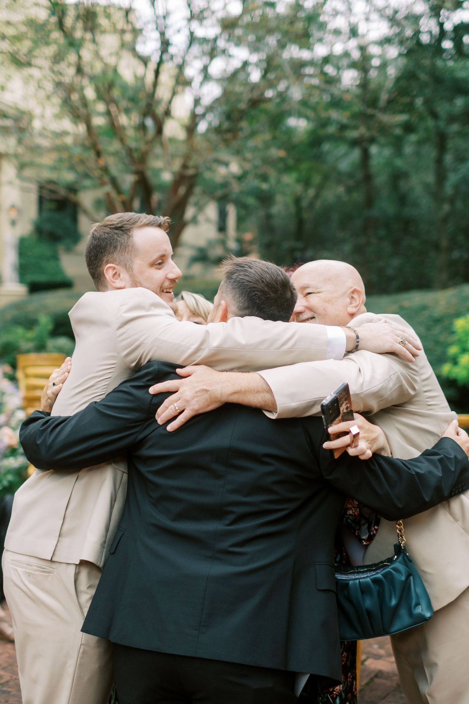 Groomsmen share emotional group hug during outdoor wedding celebration.