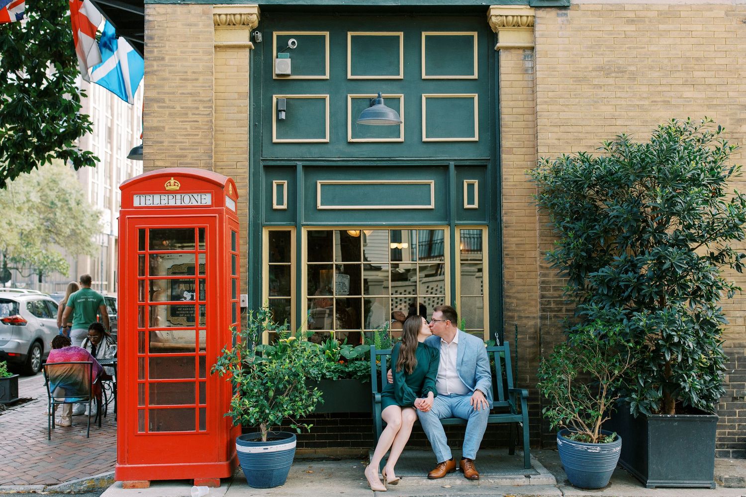 A couple sits near a classic red British phone booth outside a teal storefront.