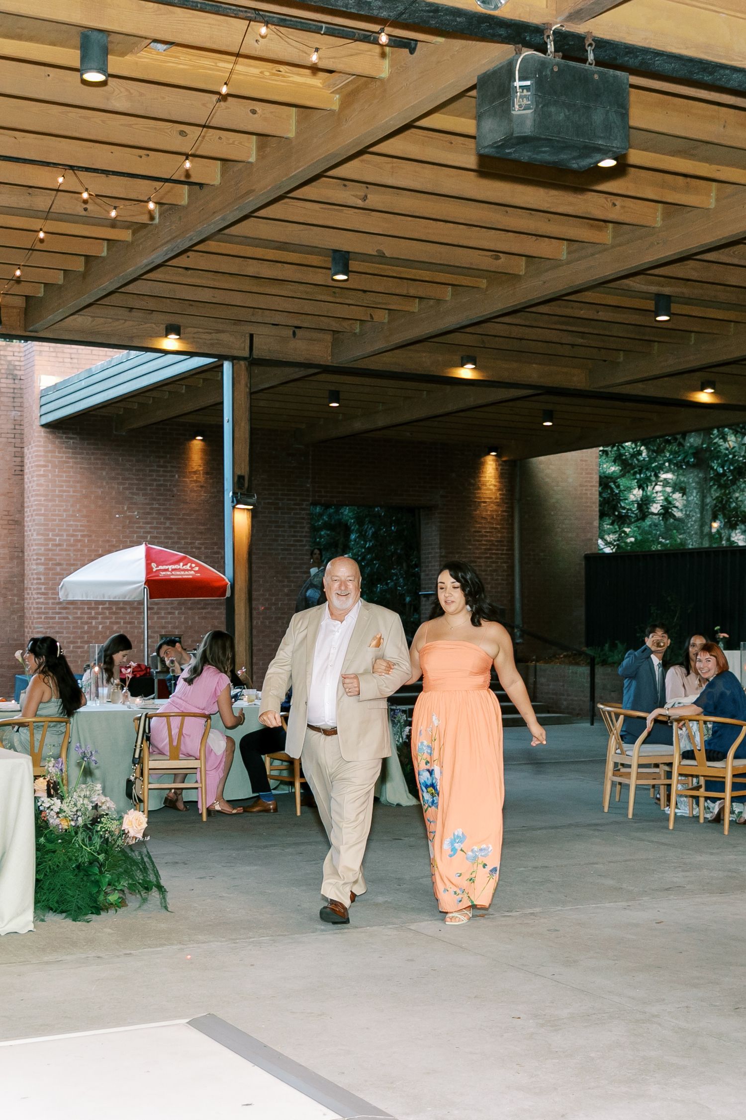 Wedding reception setup under a covered outdoor pavilion with scattered tables and chairs.