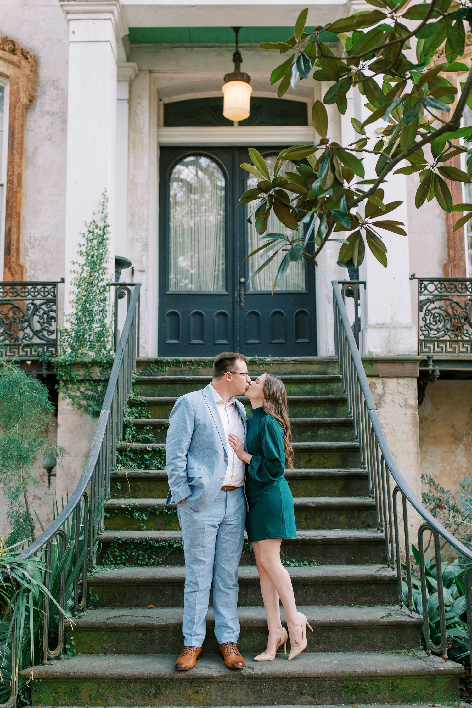 A couple embraces on historic stone steps with ornate railings and a green vintage door.