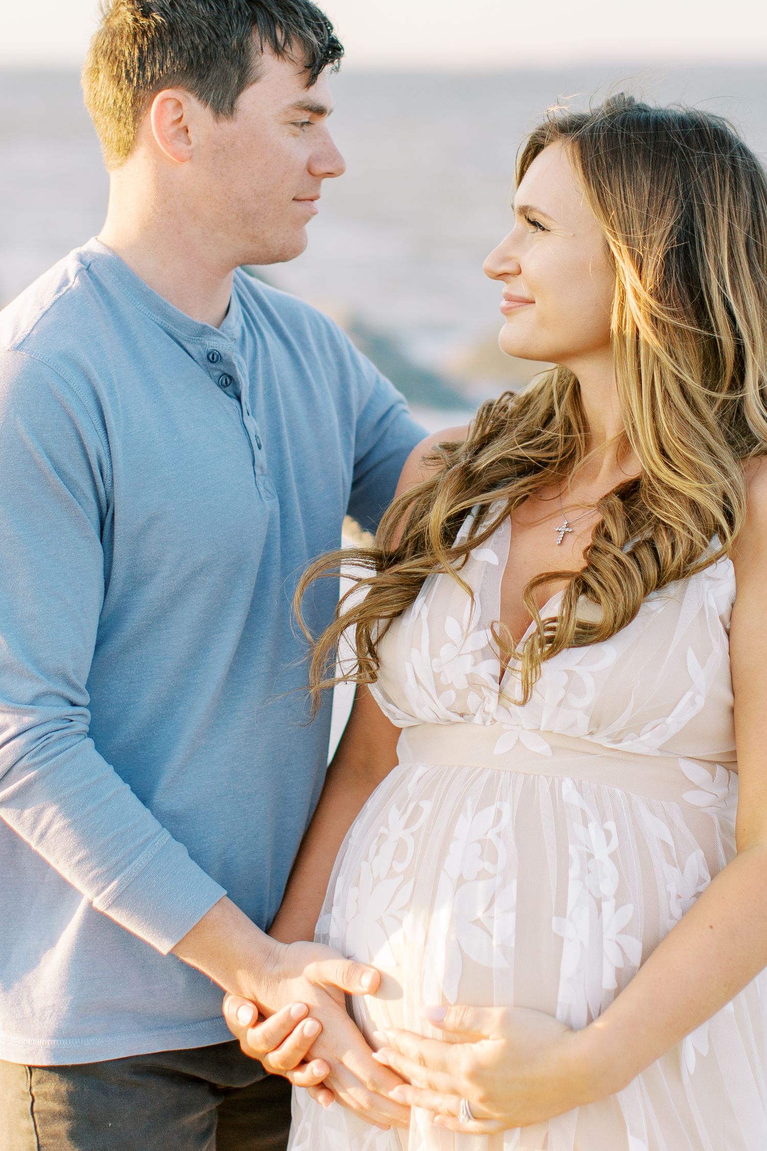 A romantic maternity photo shows a couple in casual attire sharing a tender moment outdoors.