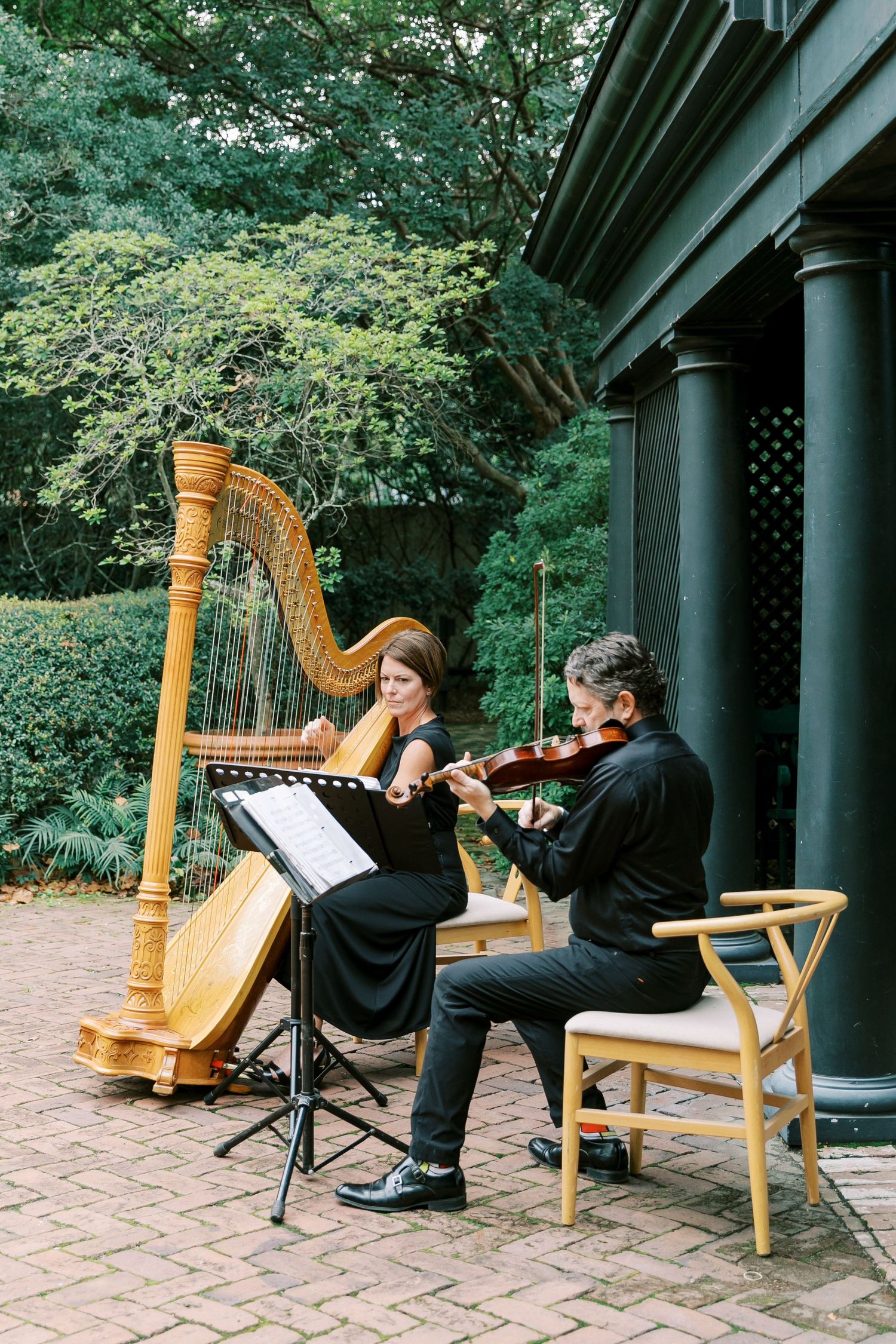 Musicians with harps perform under covered outdoor venue with brick flooring.