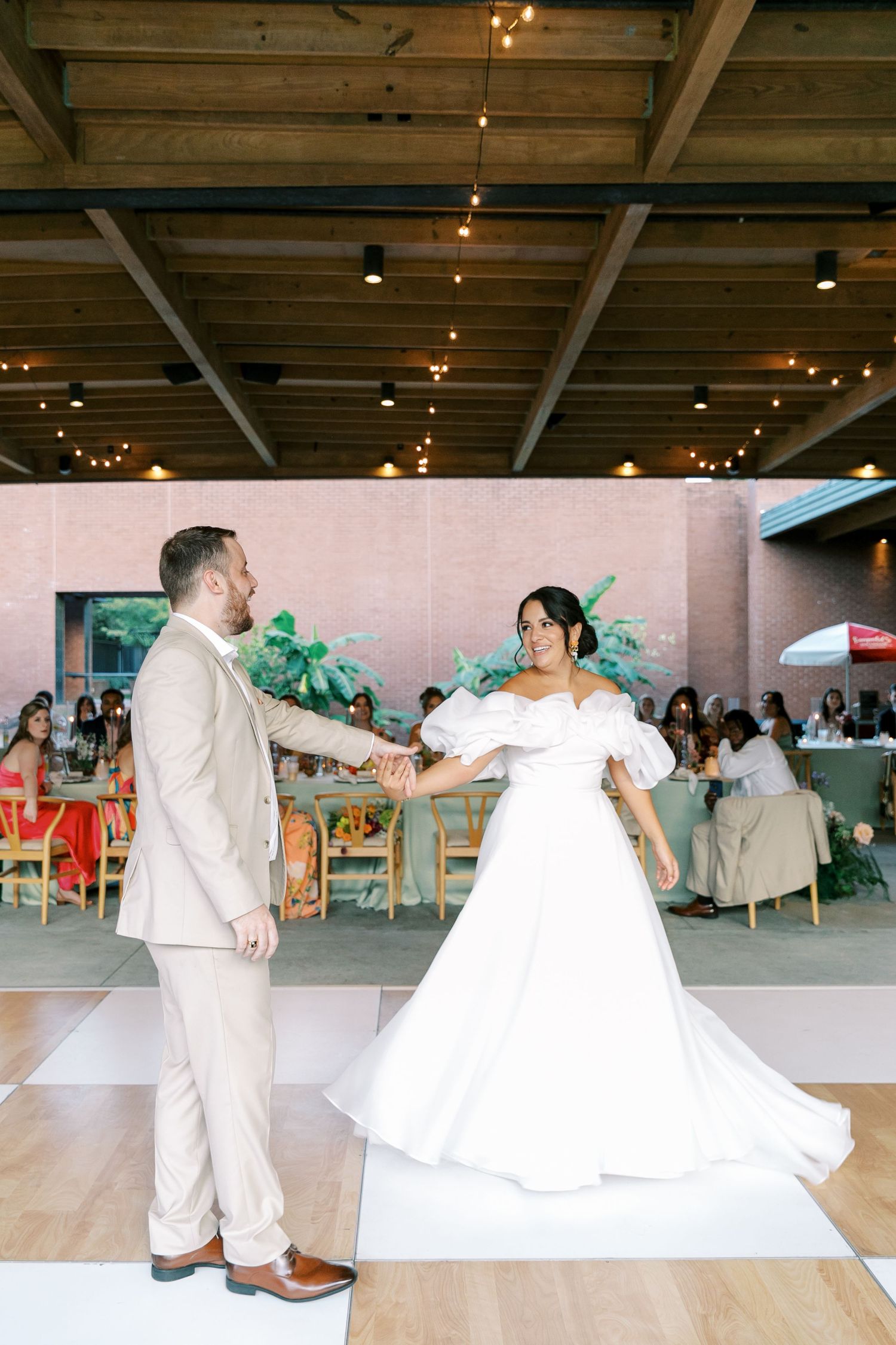 Newlyweds perform their first dance on a spacious indoor dance floor with soft lighting overhead.