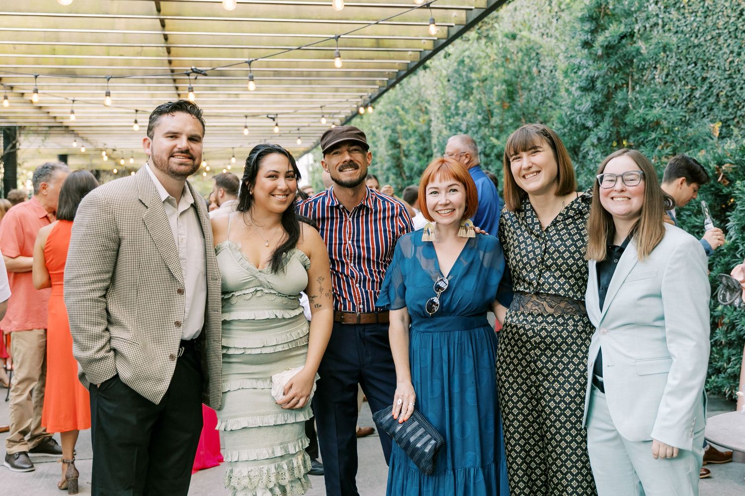 Group of wedding guests pose together at an outdoor celebration under string lights.