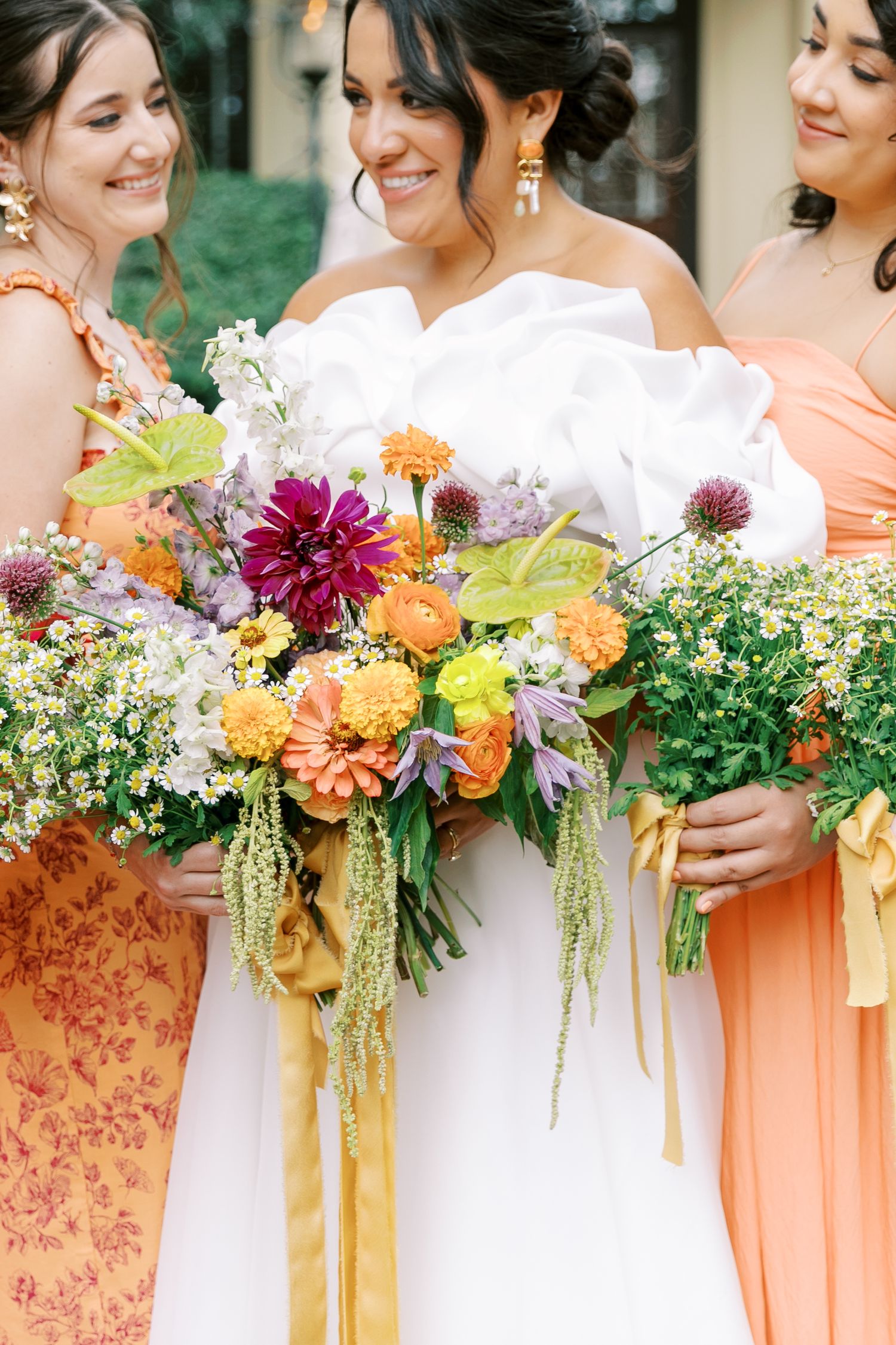 Wedding party holds stunning bouquets featuring orange, burgundy and yellow flowers with cascading ribbons.