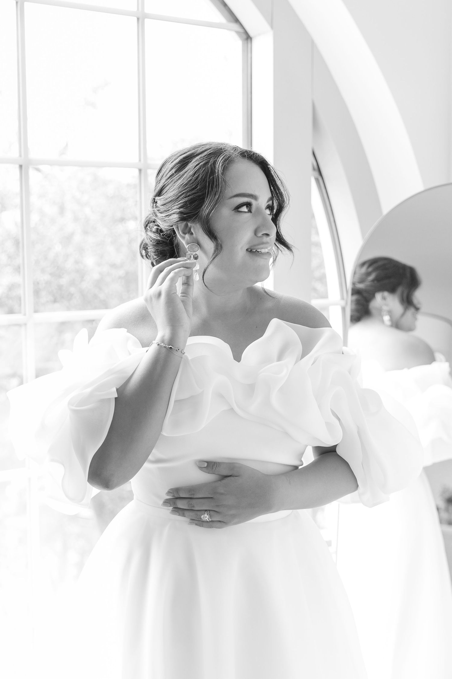 Bride in white dress poses elegantly near bright windows in a photography series.