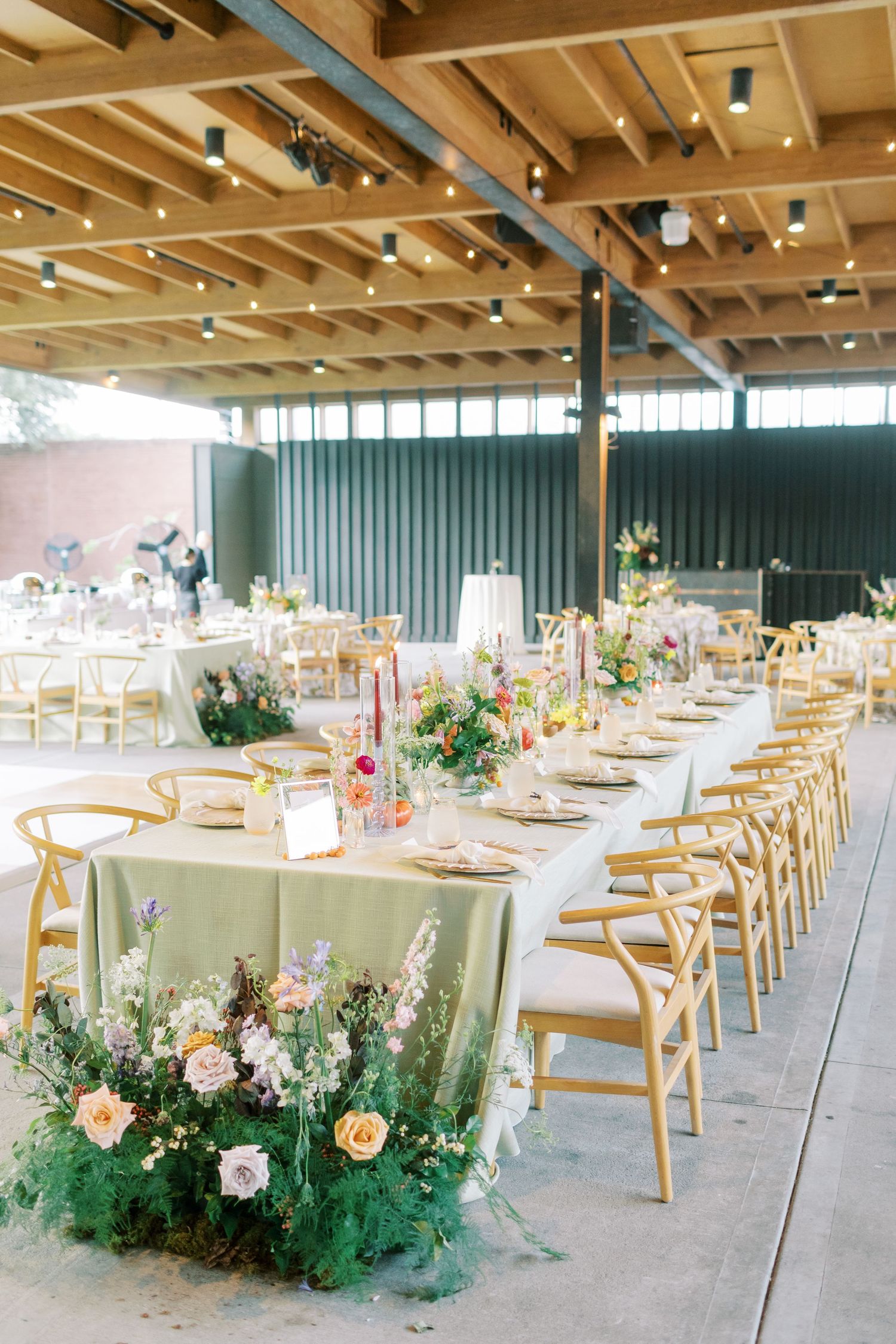 Elegant wedding reception setup with long tables, wooden chairs and fresh floral centerpieces.